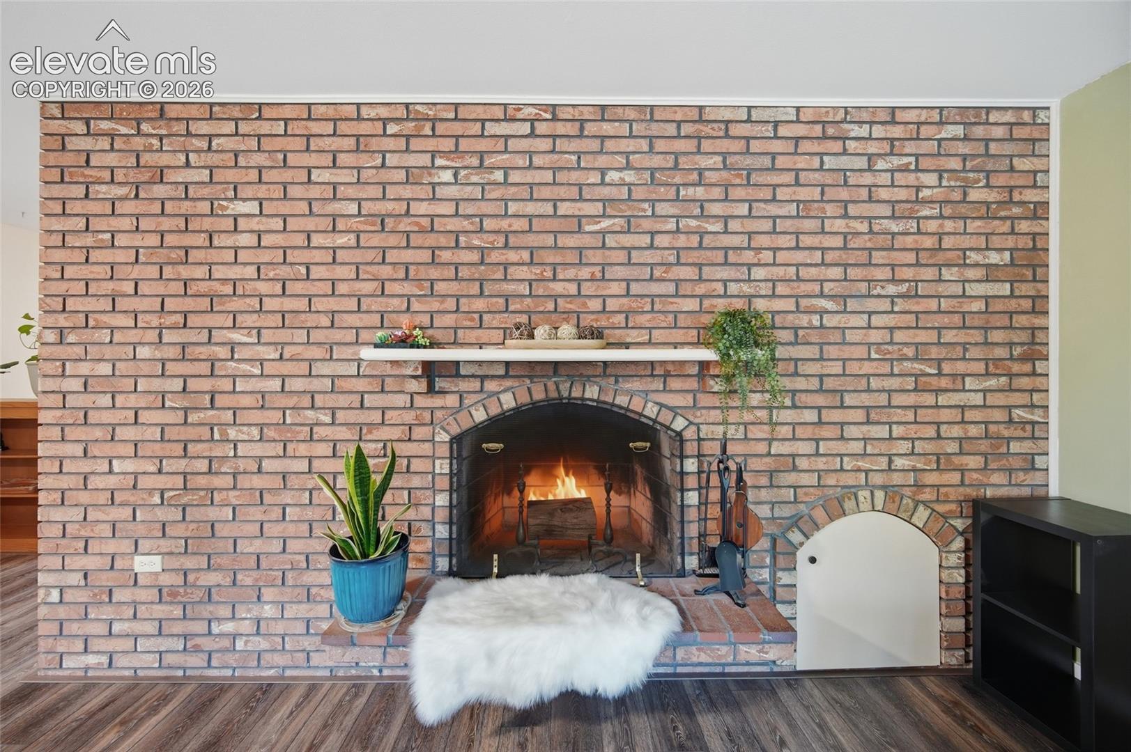 Full-height brick fireplace featuring an arched firebox, a raised brick hearth, a built-in wood storage nook with an arched header, and a horizontal mantel