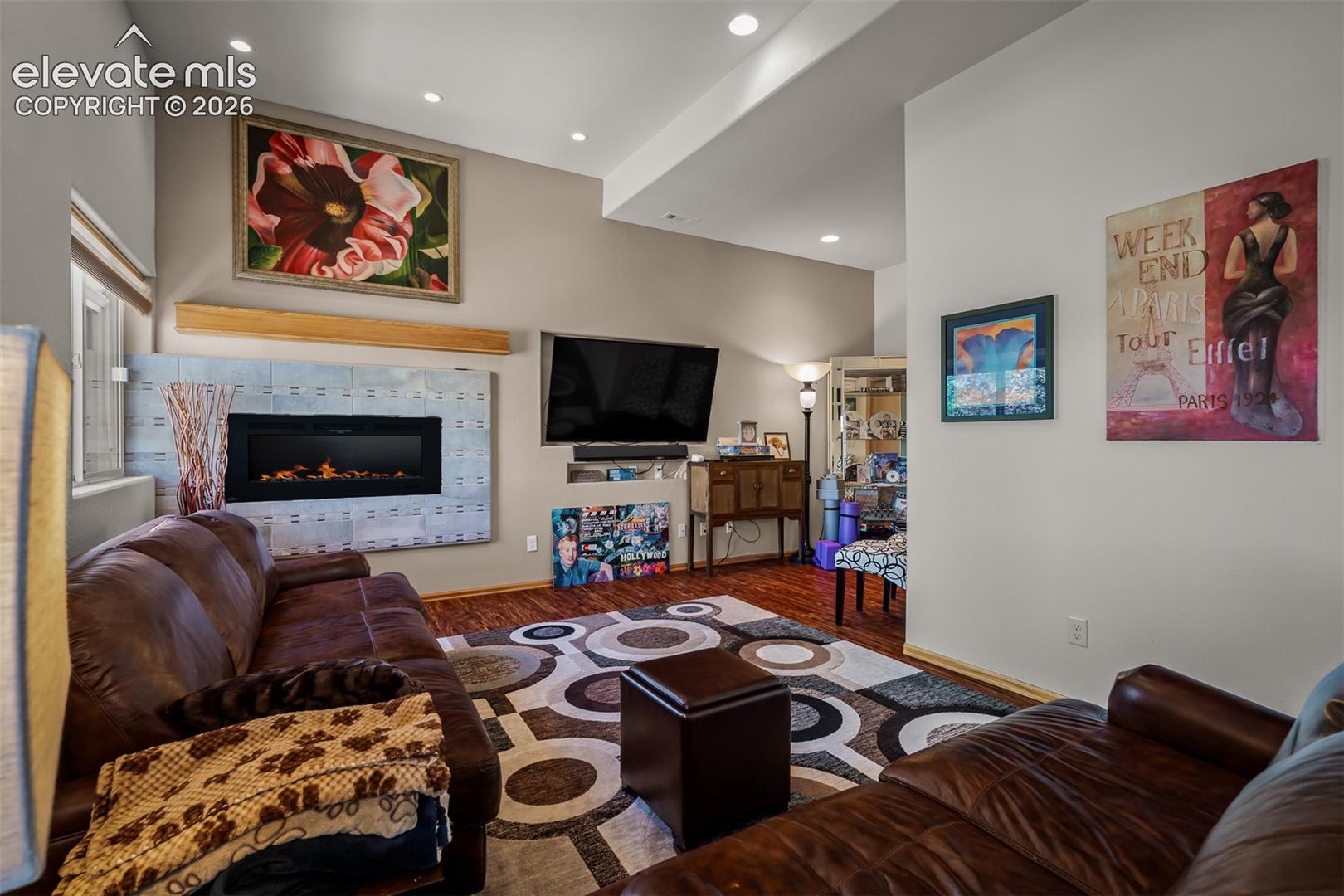 Lower level family area featuring wood-finish flooring, recessed lighting, and a prominent electric fireplace with a tiled surround, built in speakers for surrond sound and 12' ceiling.