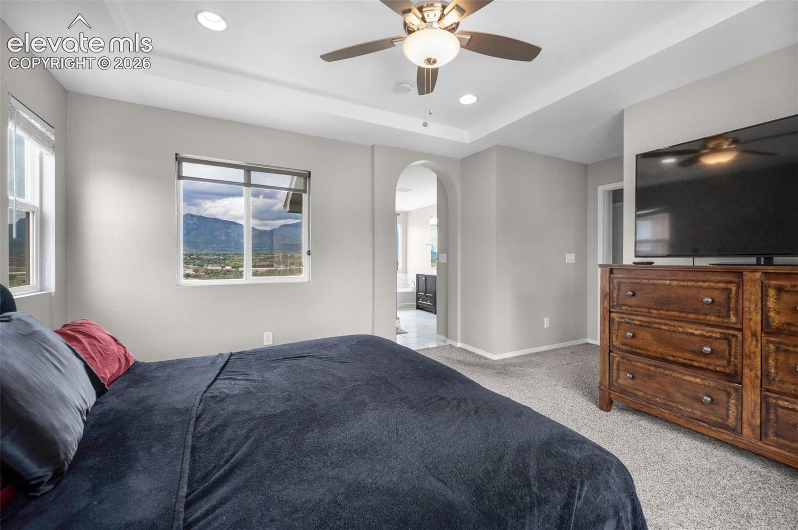 Tray ceiling with recessed lighting and ceiling fan. The primary bath doorway is in the background