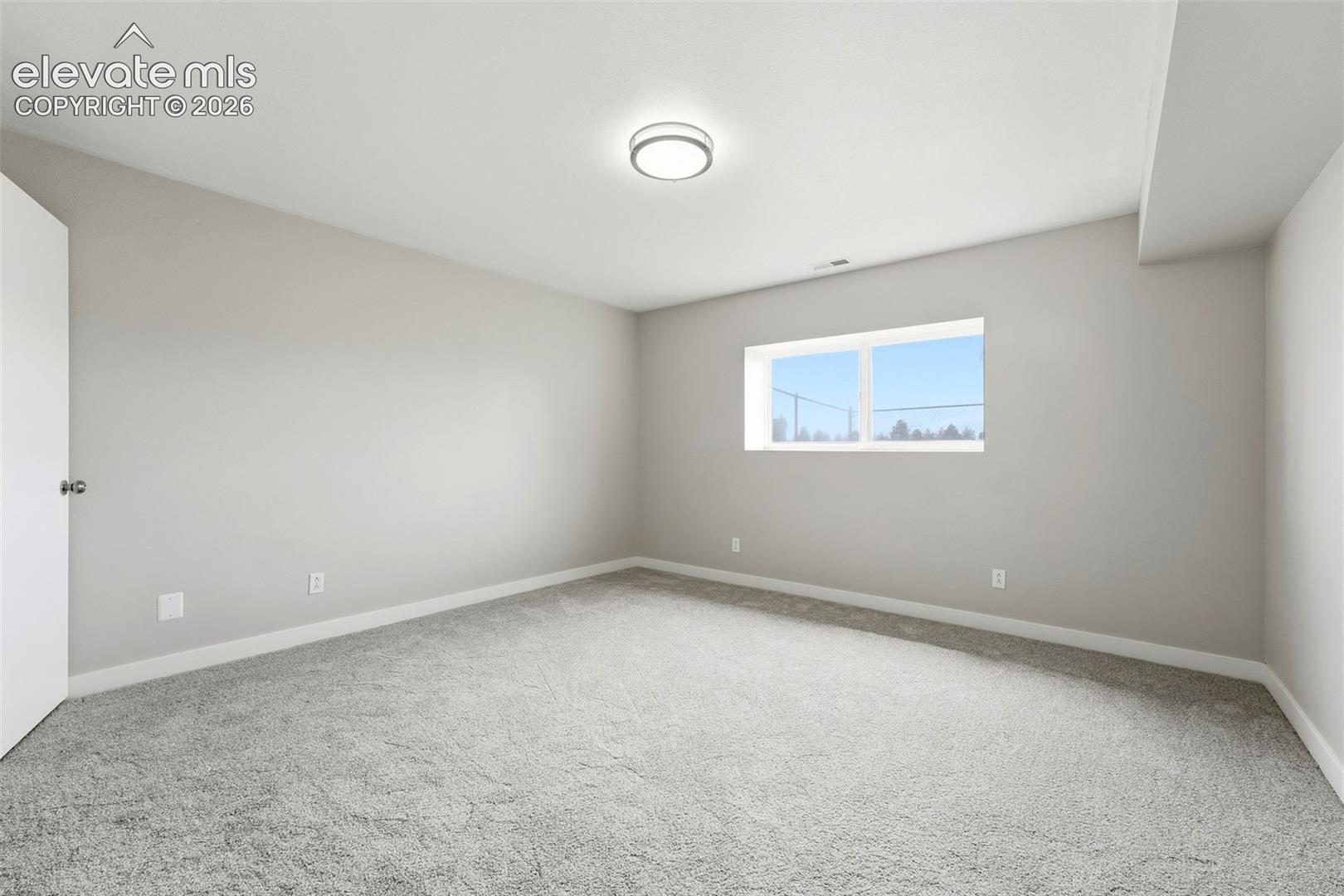 Wall-to-wall carpeting in a neutral tone, flush-mount ceiling light, white trim, and a horizontal window