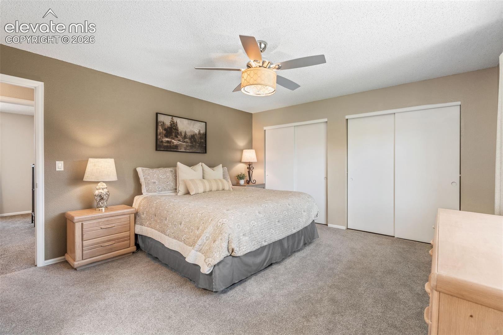 Bedroom interior featuring neutral wall paint, dual sliding closet doors, wall-to-wall carpeting, and a central ceiling fan with an integrated light fixture
