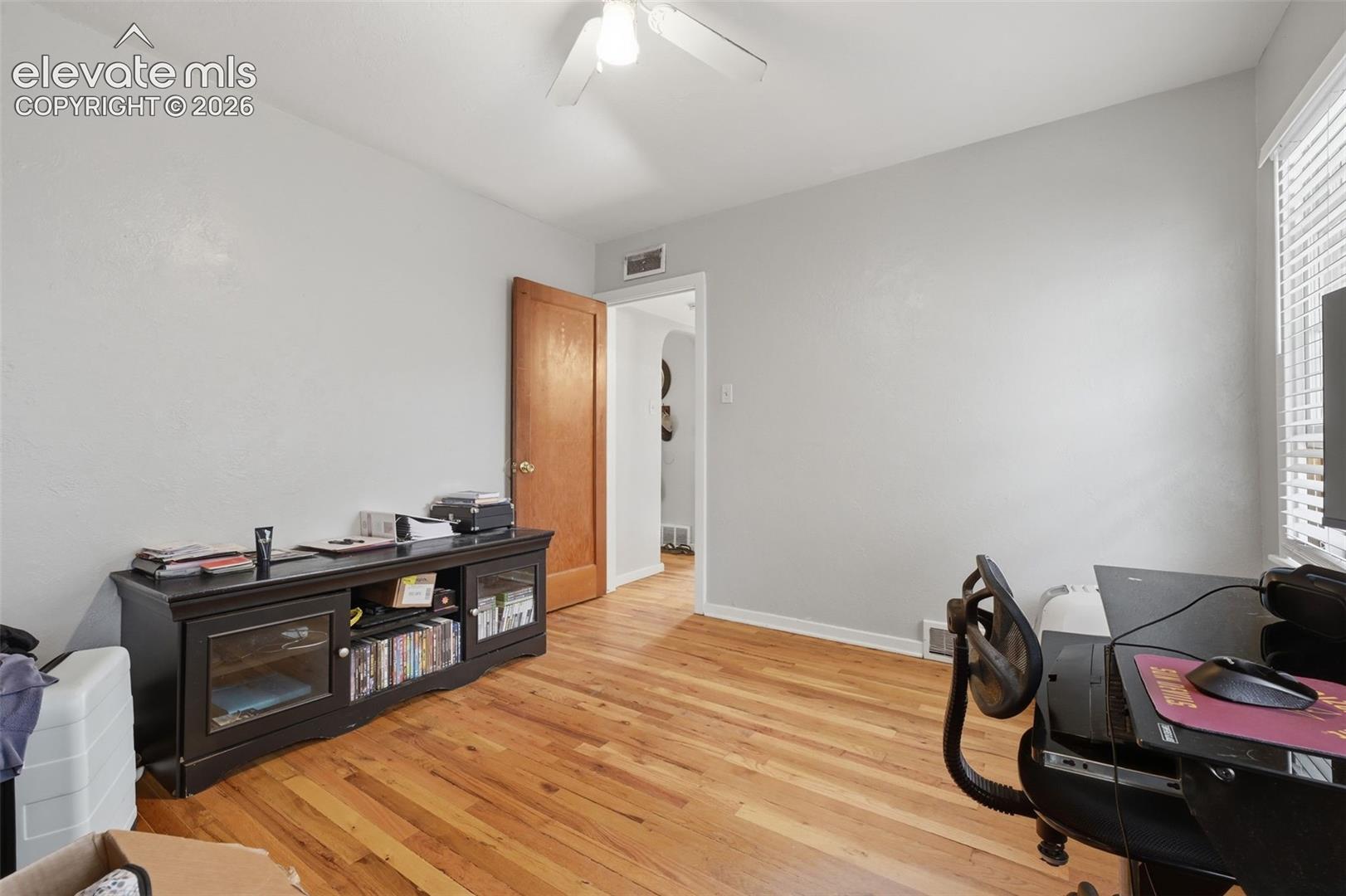 Wood-finish flooring, white ceiling fan, and window with blinds