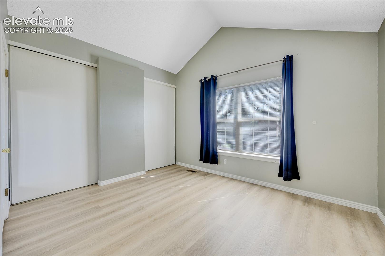 Vaulted ceiling, two sliding closet doors, wood-finish flooring, and a window with white trim