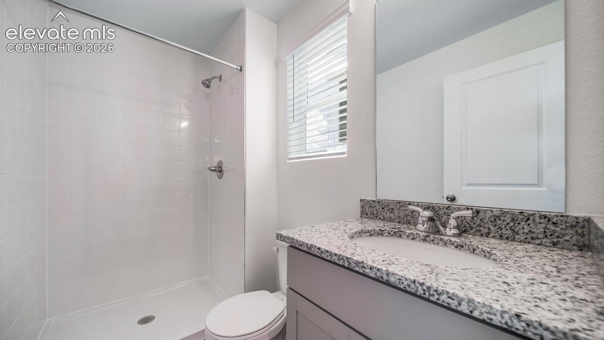 Bathroom featuring a vanity with a stone-composite countertop, an undermount sink, chrome faucet hardware, and a tiled shower enclosure
*photos of a model home*