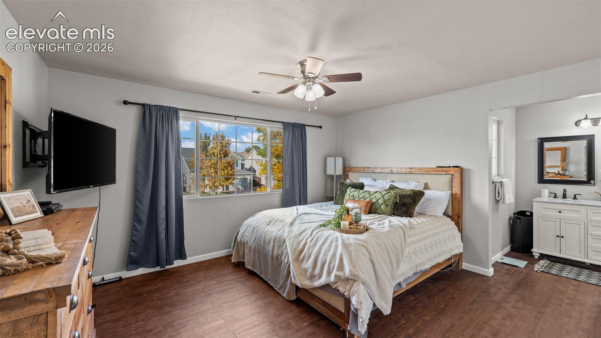 Wood-finish flooring, ceiling fan with light fixture, double pane window, white vanity with dual sinks, and wall-mounted television