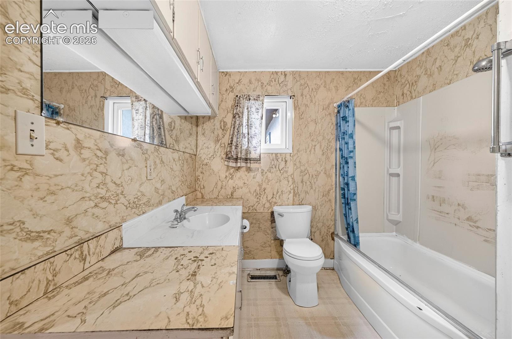 Vanity with integrated sink, wall-mounted mirror, overhead lighting fixture, built-in cabinetry, and a bathtub with shower surround