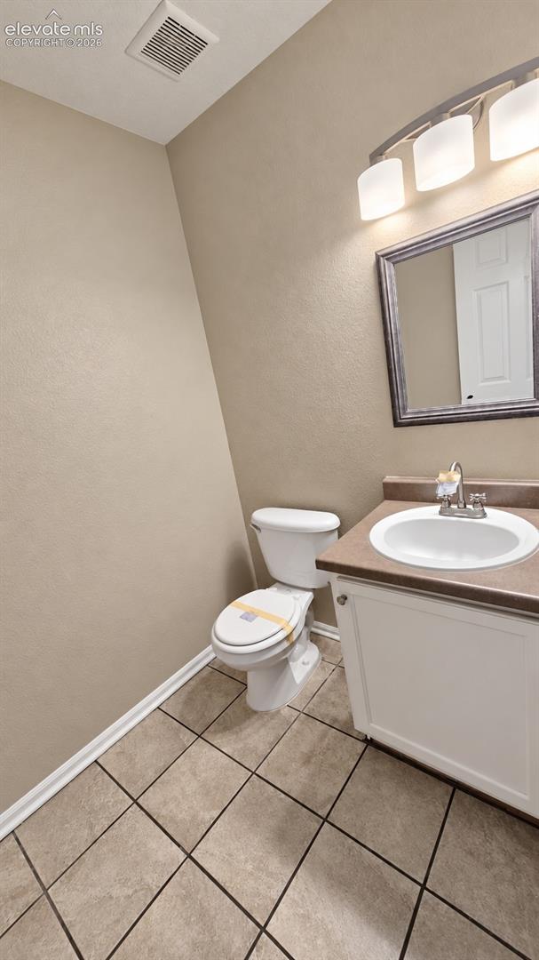 White vanity with a solid-surface countertop and integrated sink, framed wall mirror, three-light vanity fixture, and tiled flooring