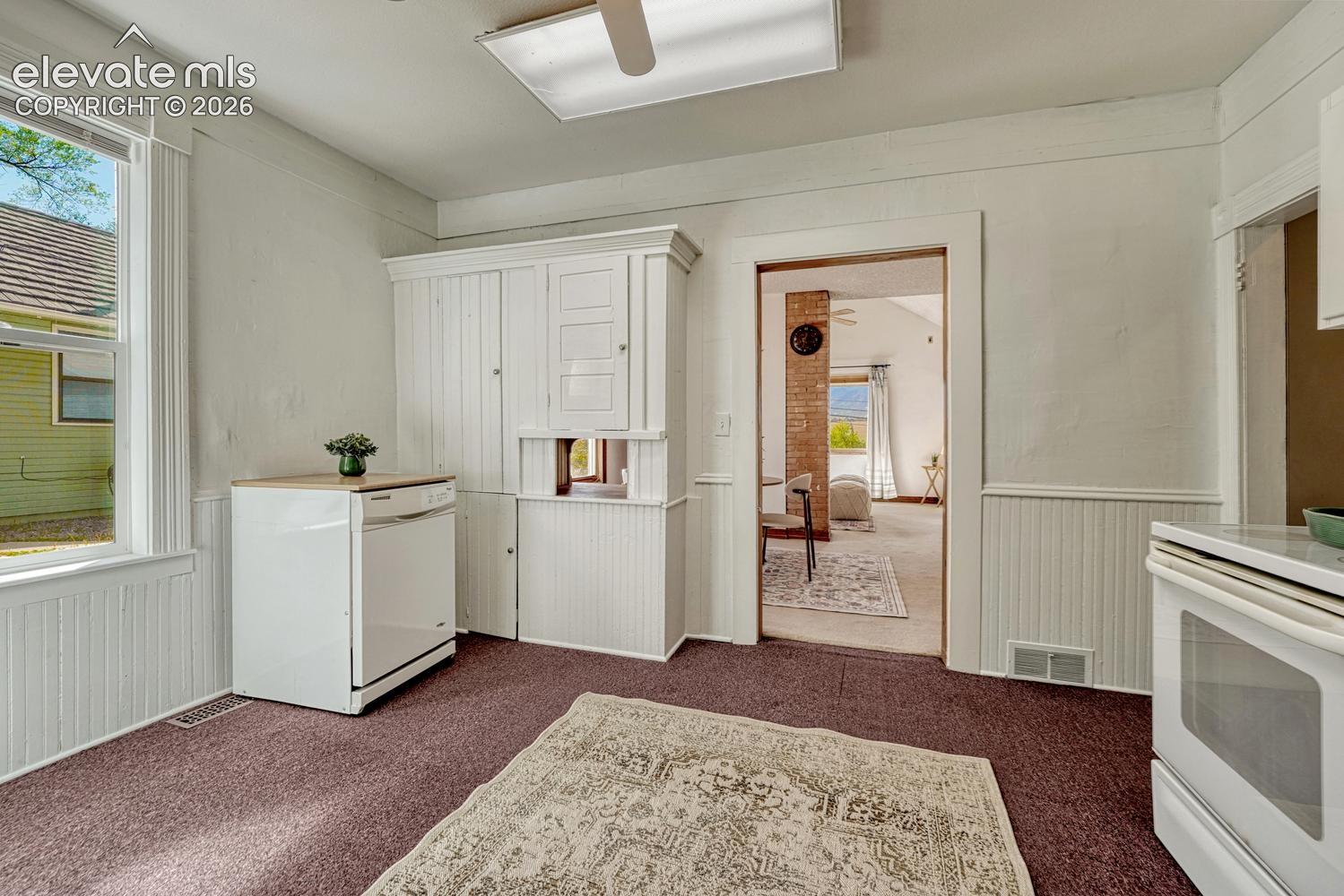 Built-in cabinetry with beadboard paneling, white appliances, and a window providing natural light