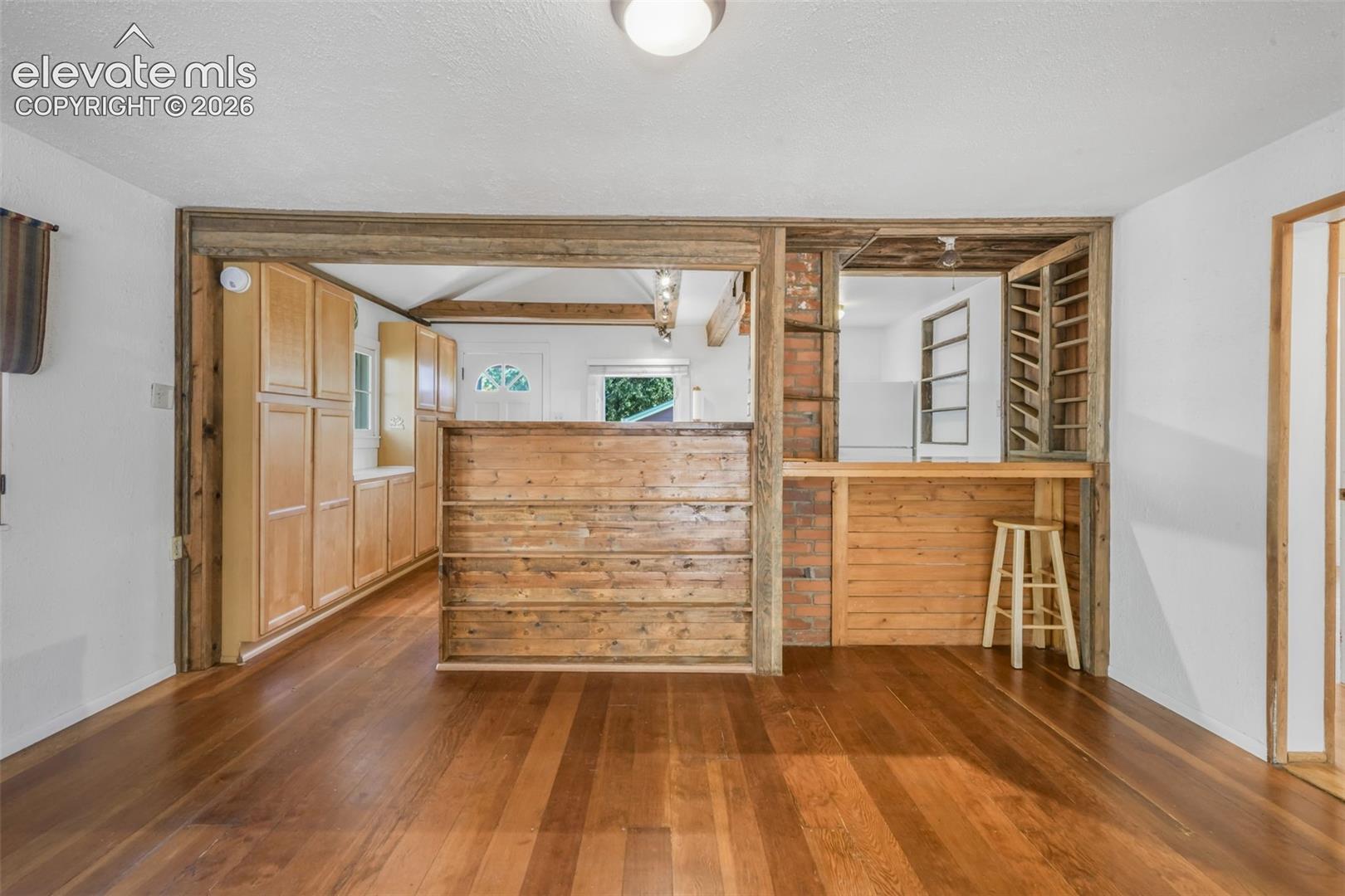 Wood-finish flooring throughout, exposed wood beams, built-in wooden cabinetry, exposed brick detailing, and a built-in bar area