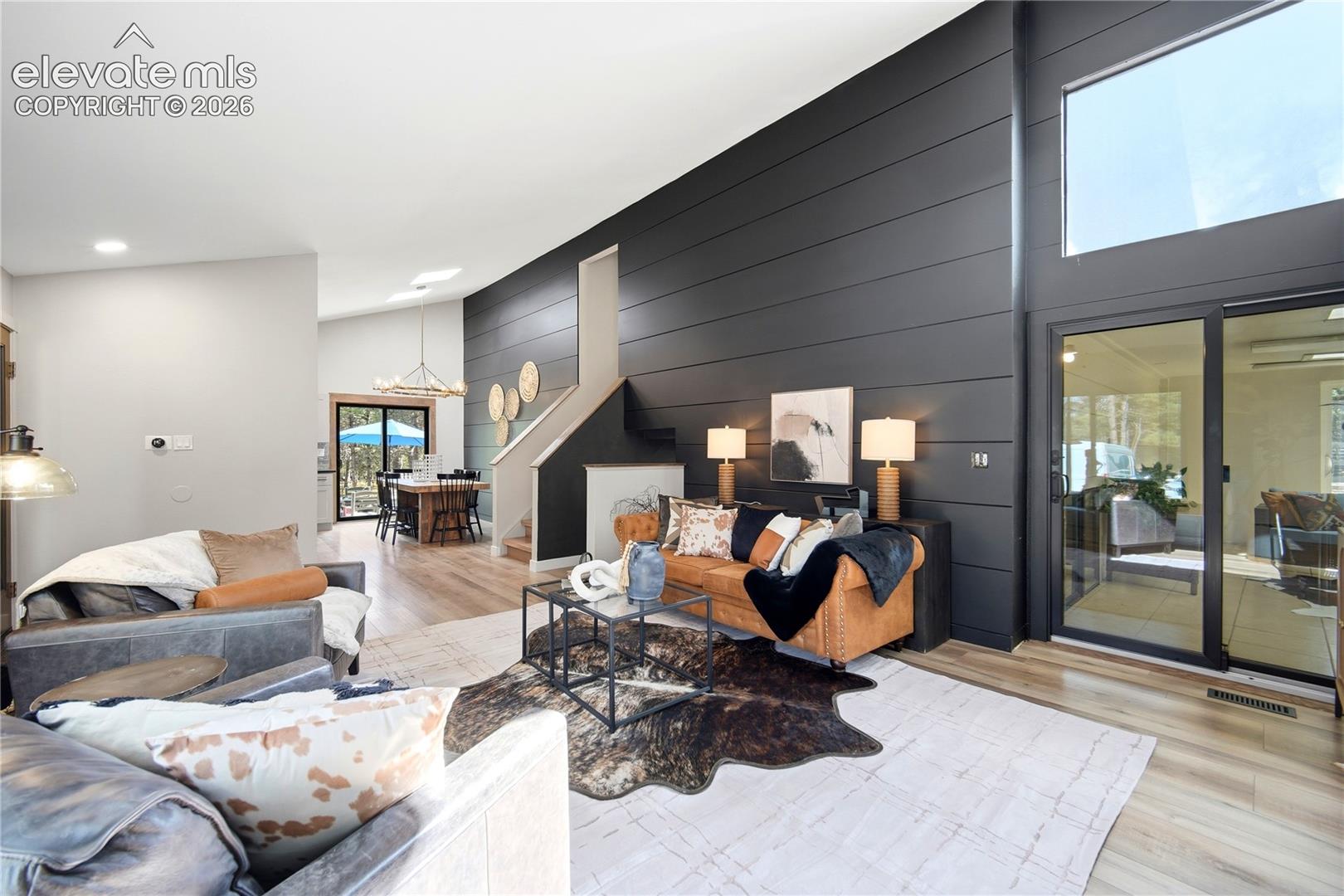 Vaulted ceilings, expansive horizontal shiplap accent wall, wood-finish flooring, sliding glass door, and large transom window
