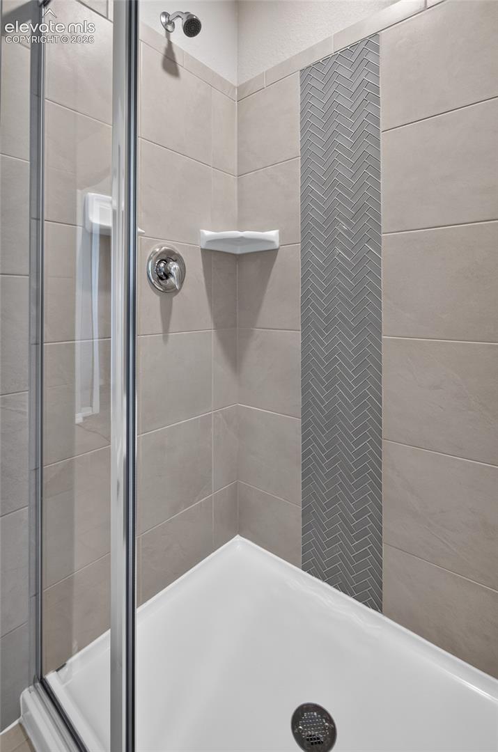 Walk-in shower enclosure featuring large-format ceramic wall tiles, a vertical herringbone tile inlay, chrome shower fixtures, and a built-in corner shelf