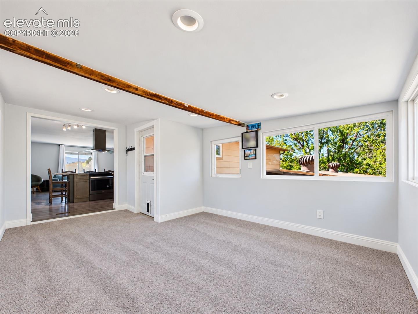 Sunroom addition directly off the kitchen features soft carpeting, recessed lighting, an exposed wood beam, and multiple windows overlooking the mature backyard greenery.