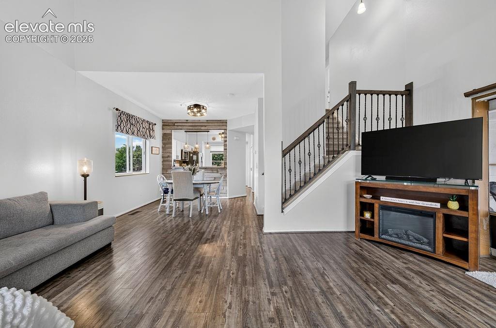 High vaulted ceilings, wood-finish flooring, staircase with dark wood banister and wrought iron spindles, dining area with accent wall, and built-in recessed lighting