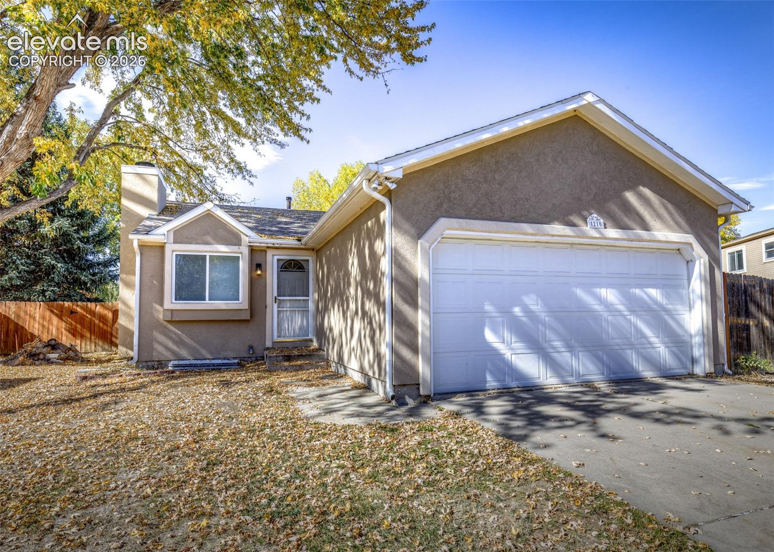 Stucco exterior featuring a dual-pitch roofline, front-facing attached two-car garage, masonry chimney, and a concrete driveway