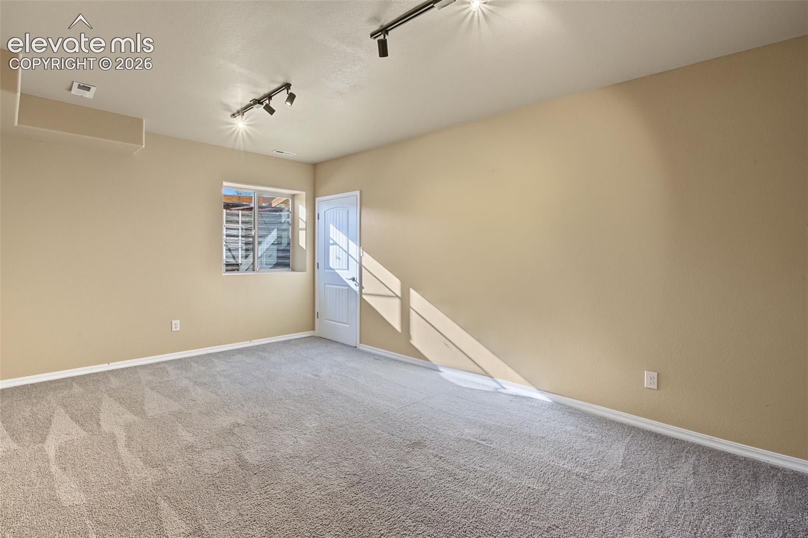 Neutral-toned interior space featuring neutral carpeting, adjustable track lighting, a recessed window, and a white paneled door