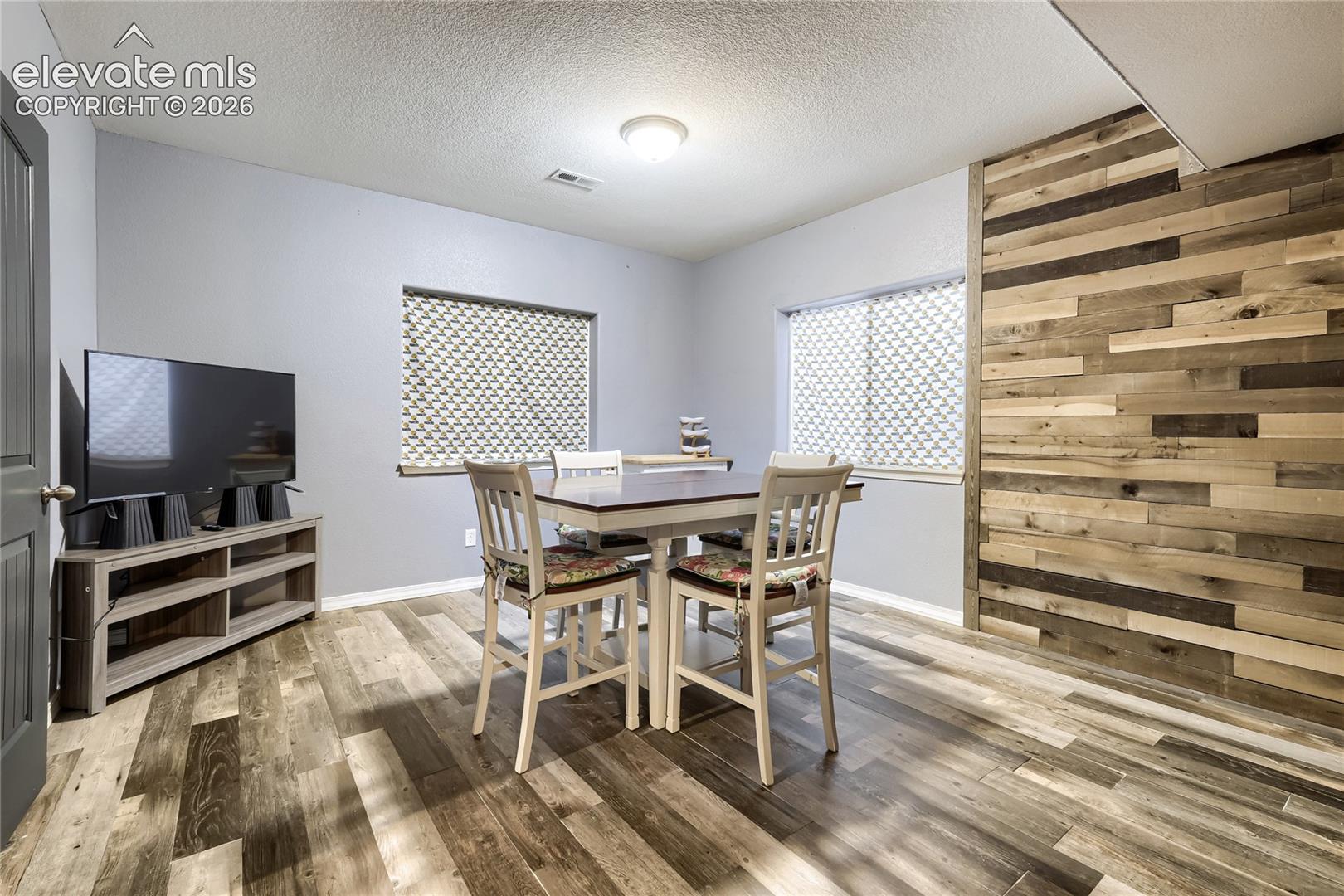 Wet bar featuring wood-finish flooring, a decorative accent wall with varied wood paneling, and neutral gray painted walls. This room adjoins the home theater room.