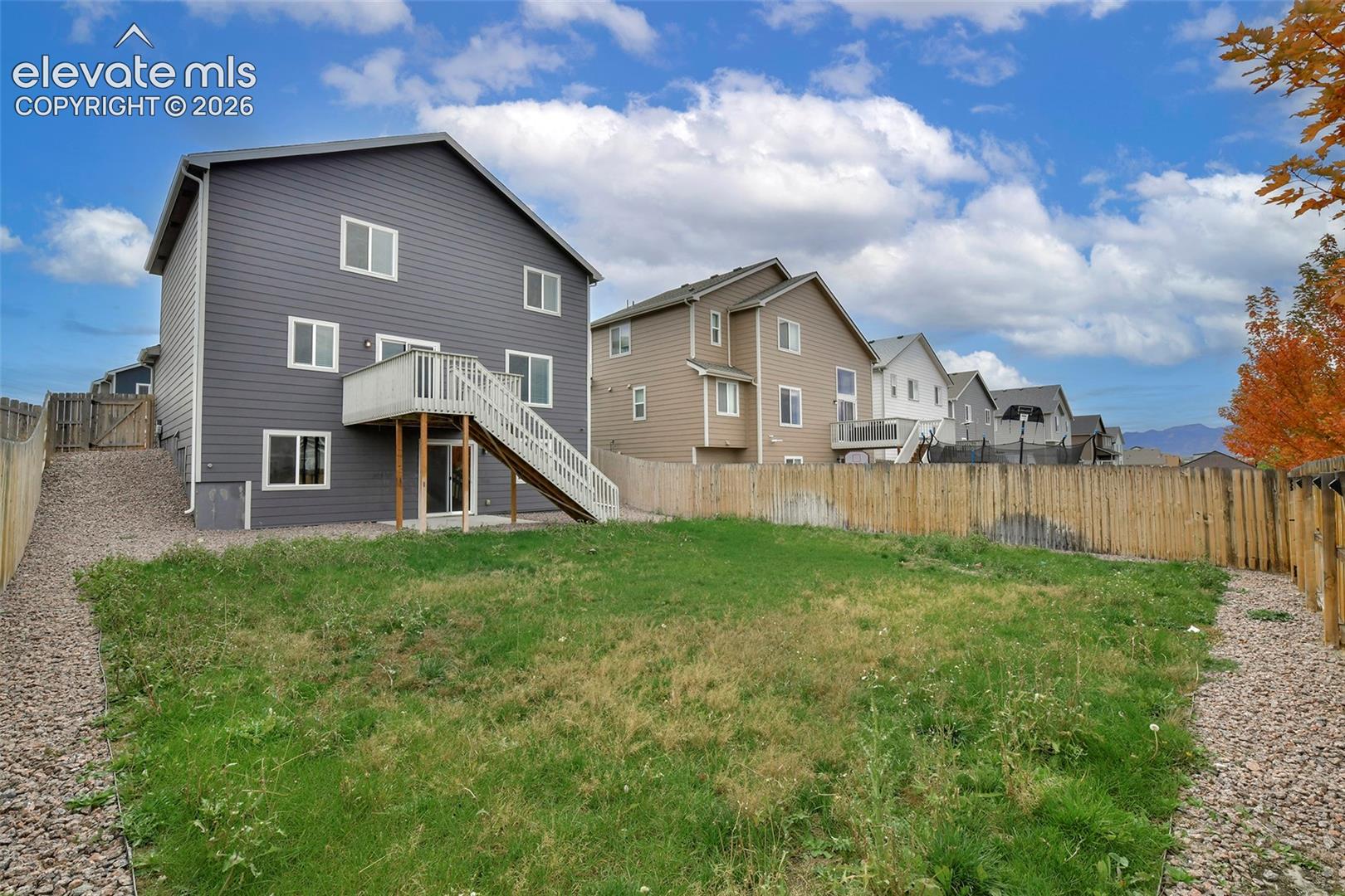 Rear exterior featuring dark horizontal siding, elevated wood deck with stairs, fenced perimeter, and crushed stone side yard