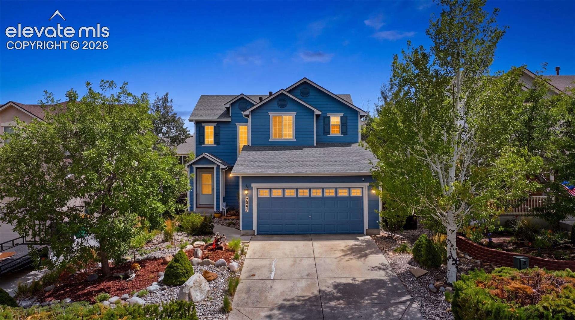 Two-story residence featuring a two-car garage, mature landscaping, and a concrete driveway