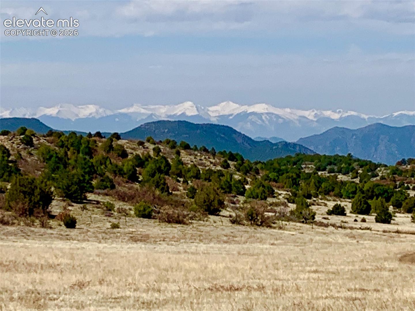 Expansive topography featuring rolling hills, native vegetation, and a prominent backdrop of snow-capped mountains