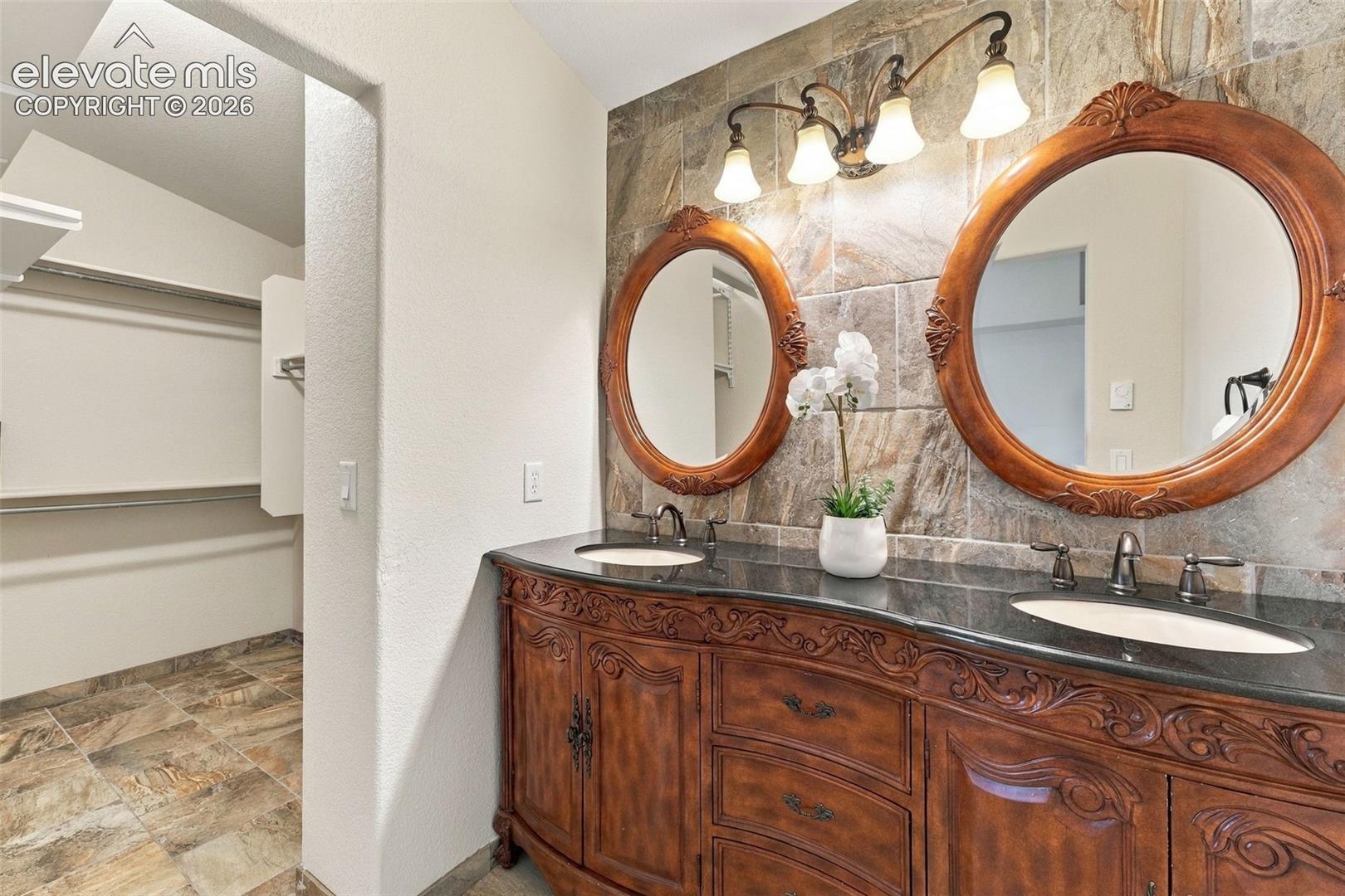 Double vanity featuring a dark stone countertop, ornate wood cabinetry, integrated oval sinks, and a decorative tile backsplash