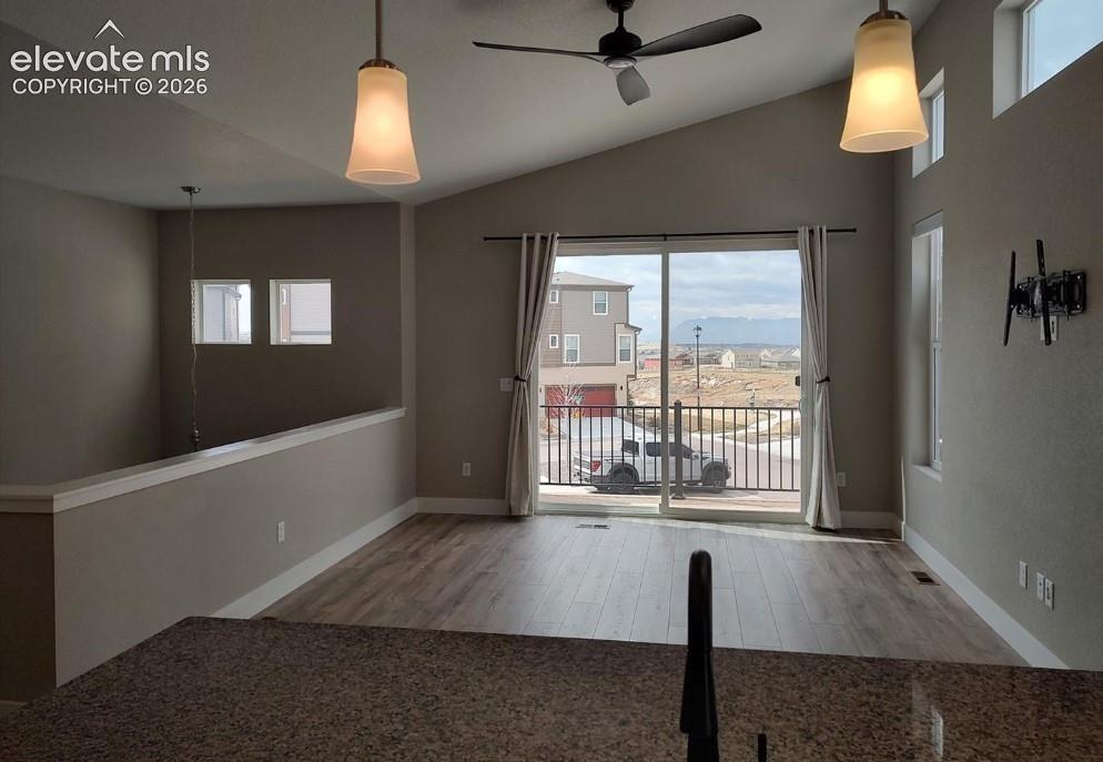 Vaulted ceilings with recessed lighting, wood-finish flooring, sliding glass door with access to a balcony, and natural stone countertops