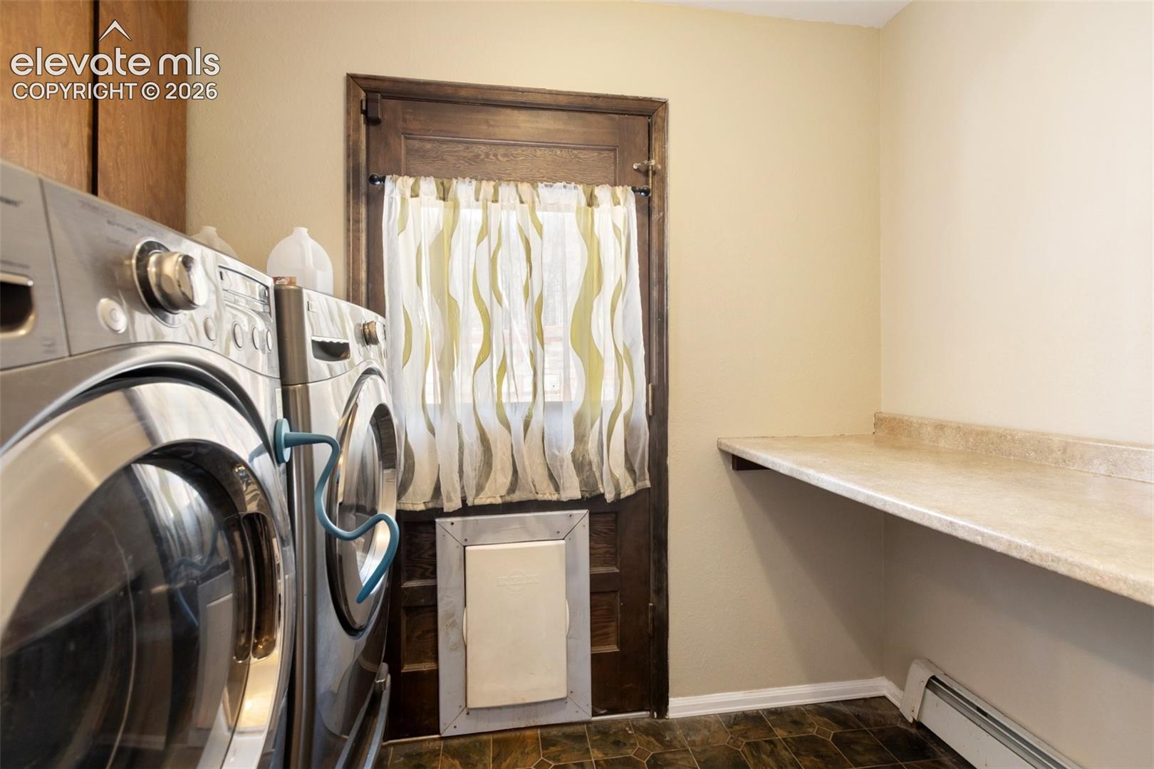 Laundry area featuring a wood-finish door, durable flooring, and built-in countertop