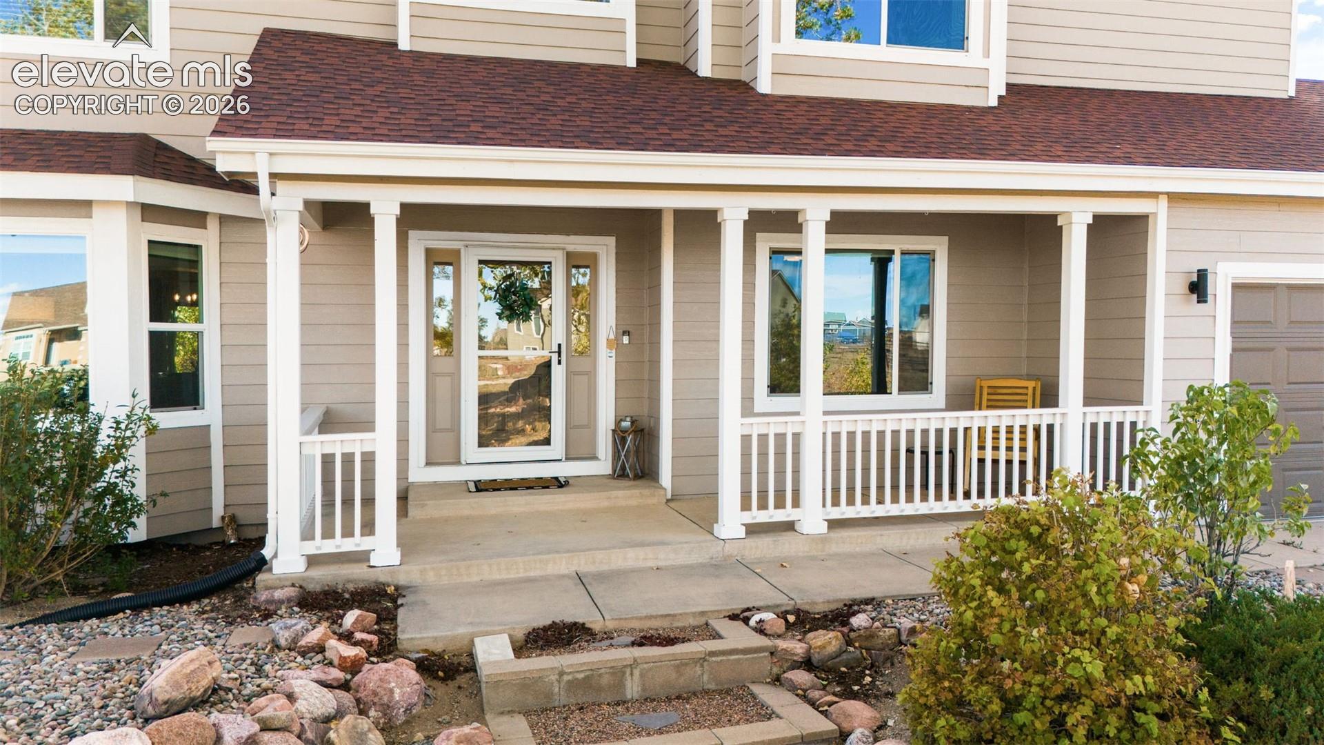 Exterior facade featuring neutral-toned horizontal siding, a covered front porch with white railing, a glass-panel entry door, and multi-paned windows