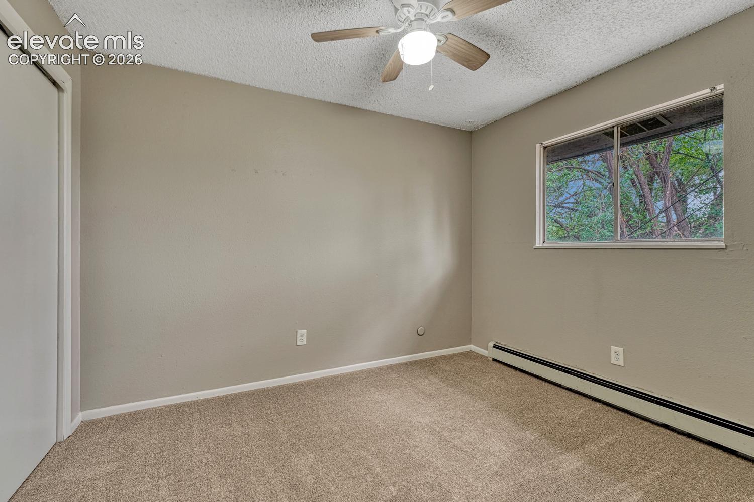 Carpeted room with a window, ceiling fan, and baseboard heating