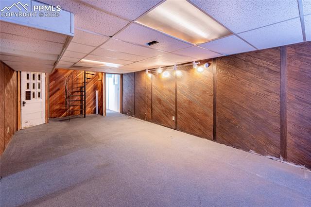 Finished below grade area featuring a paneled ceiling, stairway, wooden walls, and carpet flooring
