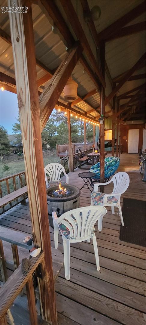 Expansive wood-decked patio with a covered metal roof, exposed wood beams, and string lighting