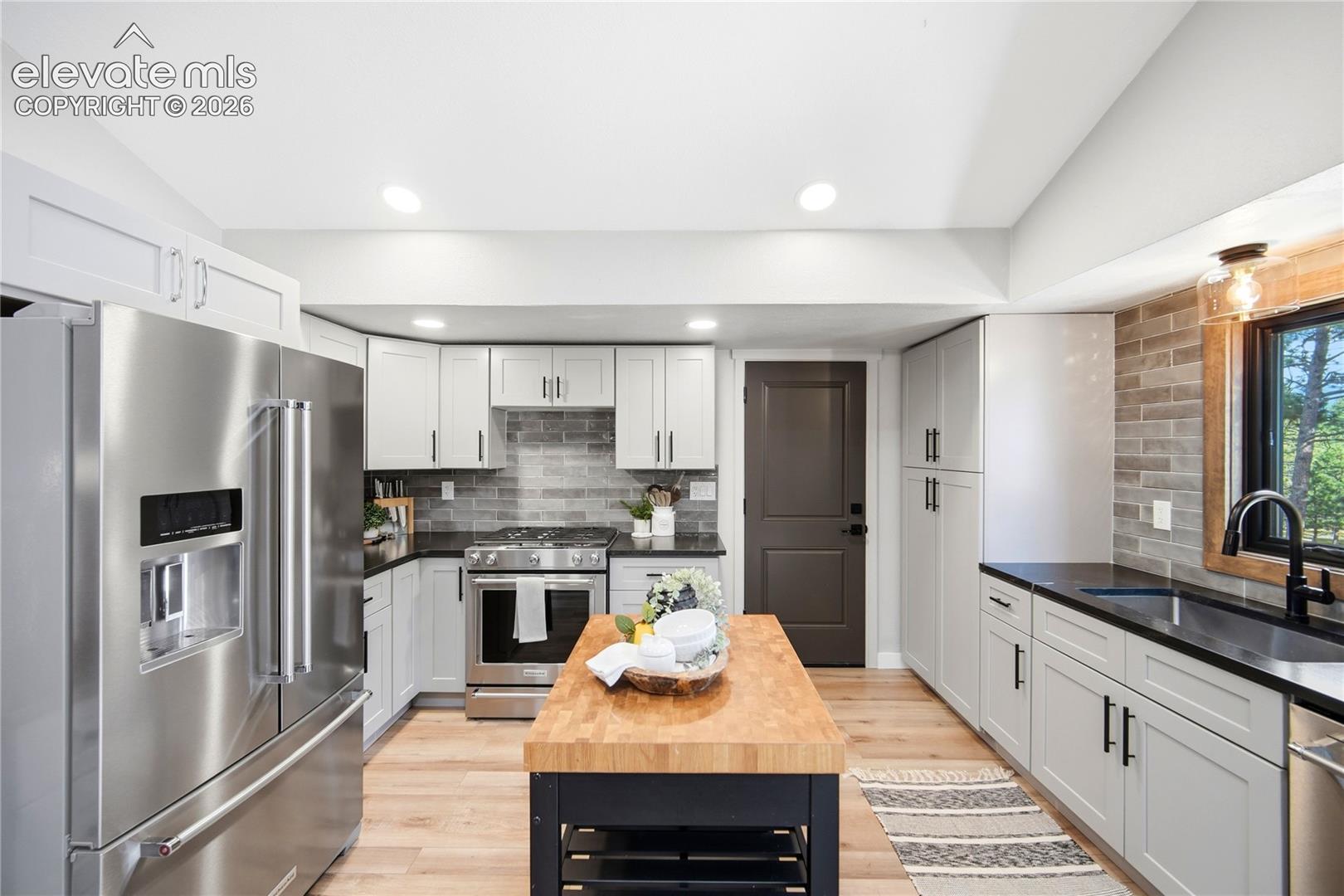 Kitchen featuring white Shaker-style cabinetry, dark countertops, subway tile backsplash, wood-finish flooring, and stainless steel appliances