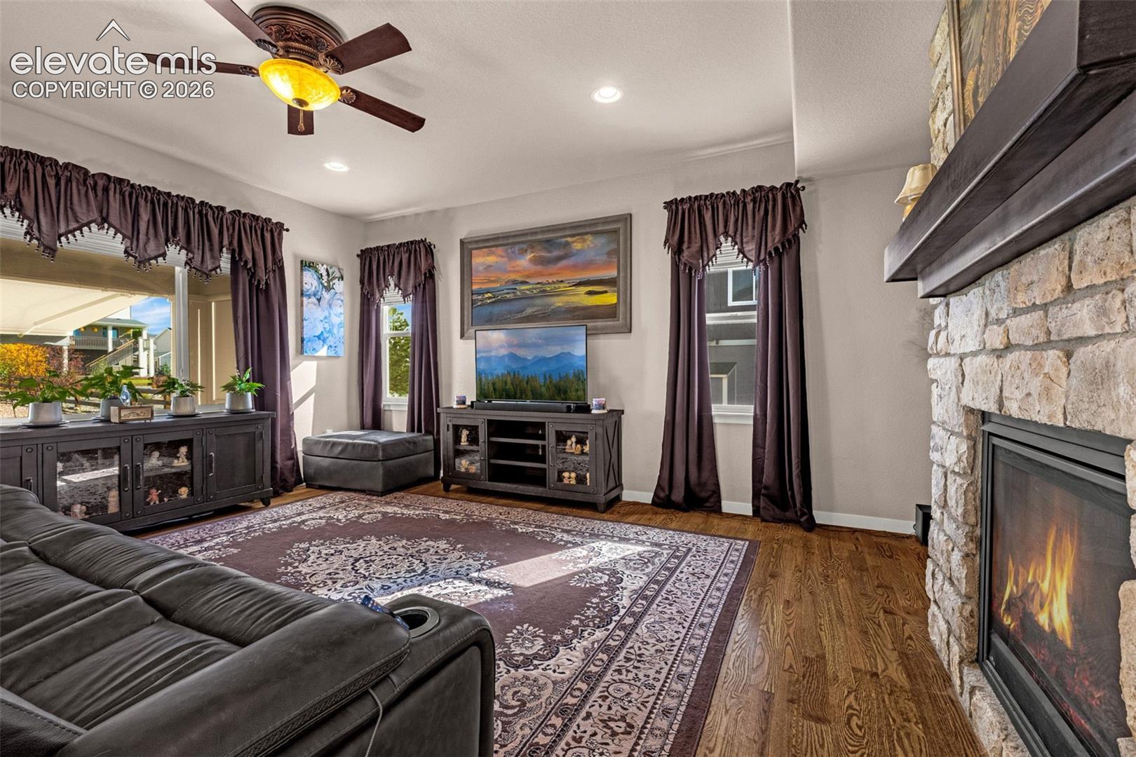 Living room featuring wood-finish flooring, a floor-to-ceiling stone-surround fireplace, recessed lighting, and a ceiling fan