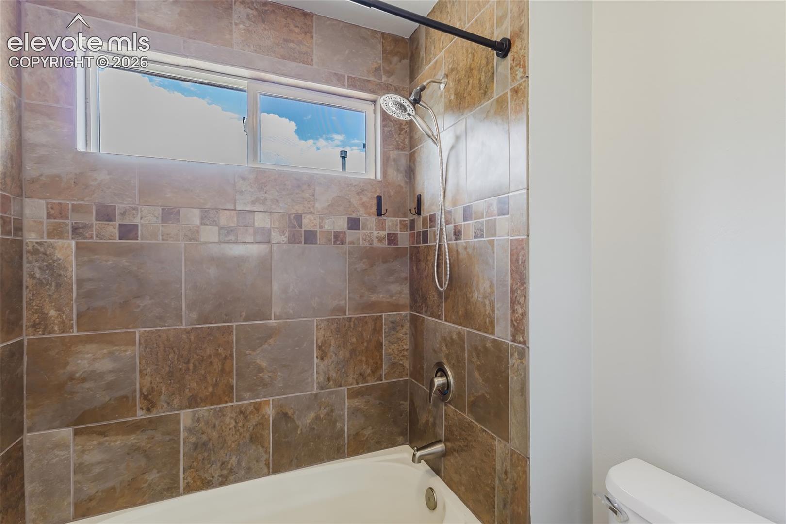 Bathtub with a tiled surround featuring a decorative accent band and a shower head with an attached sprayer