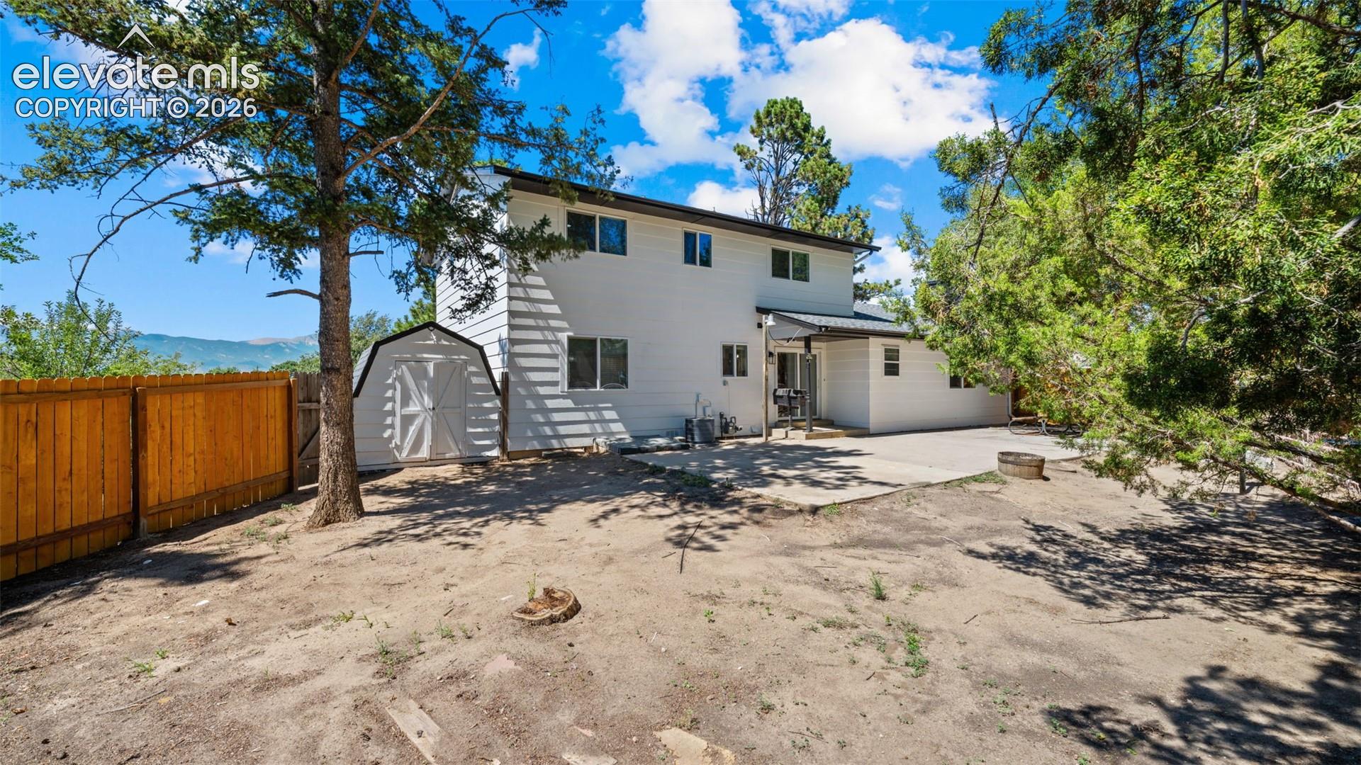 Expansive backyard featuring a privacy fence, mature trees, concrete patio, and a utility shed