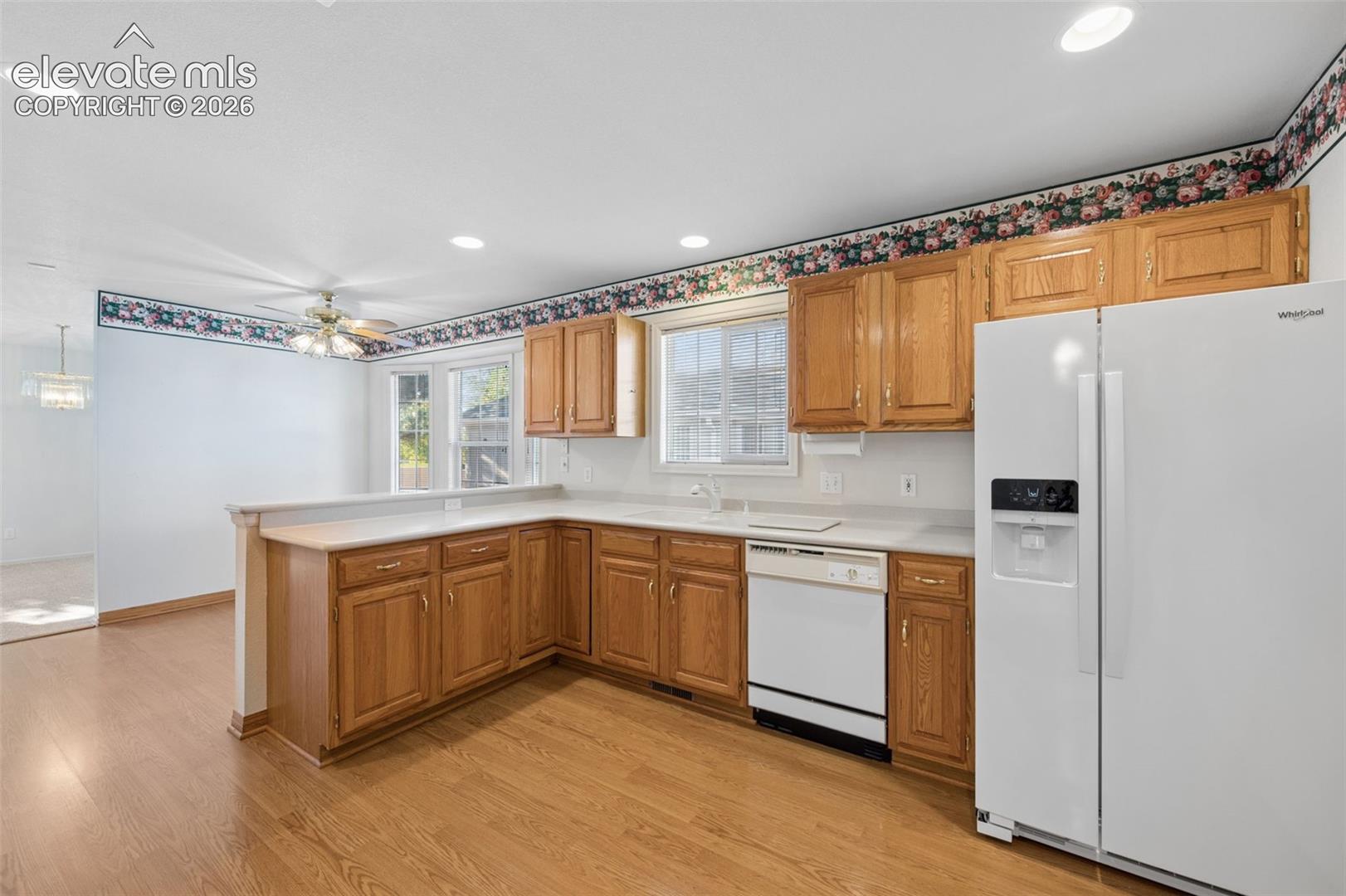 Kitchen featuring wood cabinetry, solid-surface countertops, recessed lighting, wood-finish flooring, and white built-in appliances