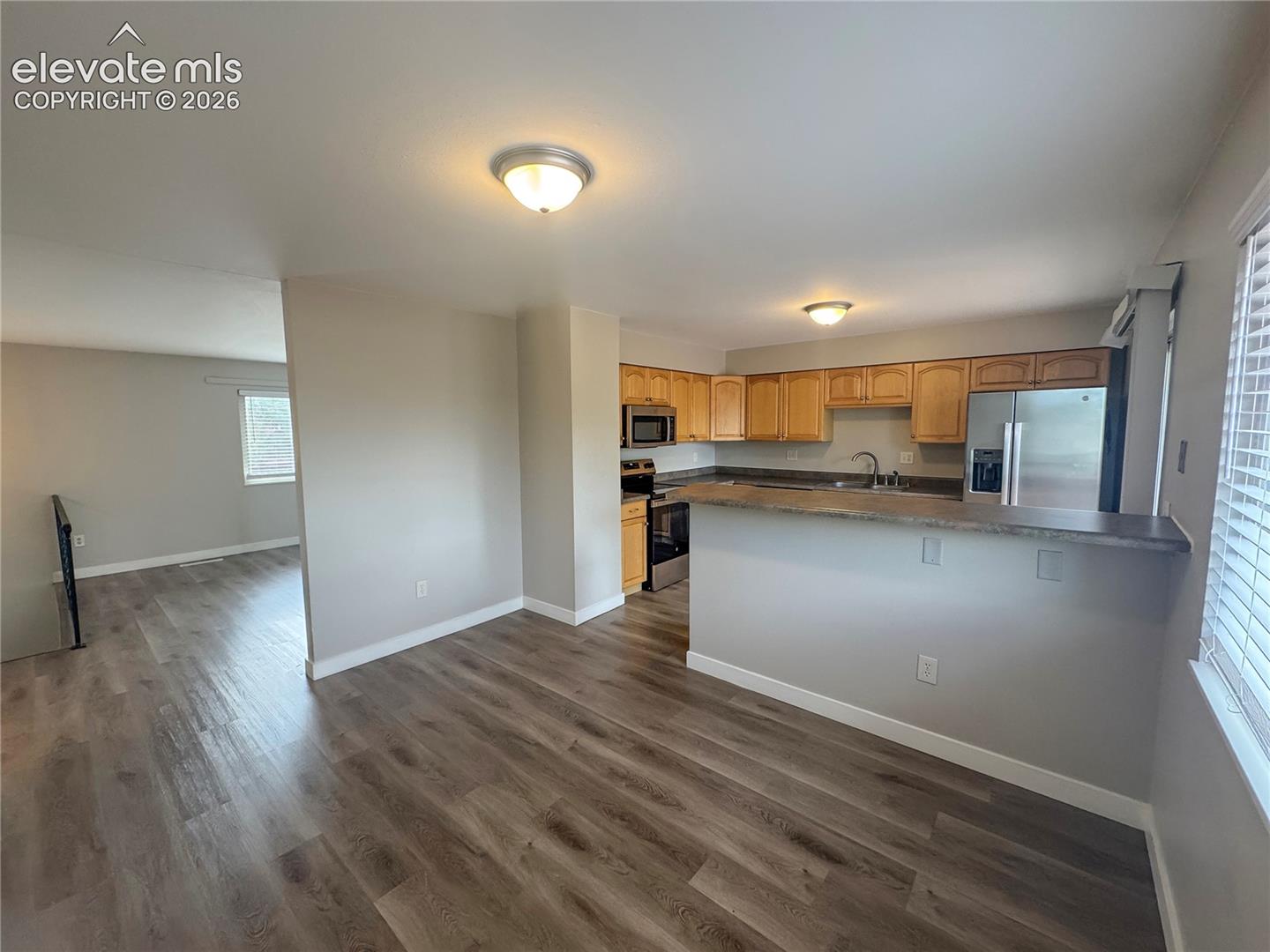 Kitchen featuring light-finish wood cabinetry, stainless steel appliances, a breakfast bar, and wood-finish flooring