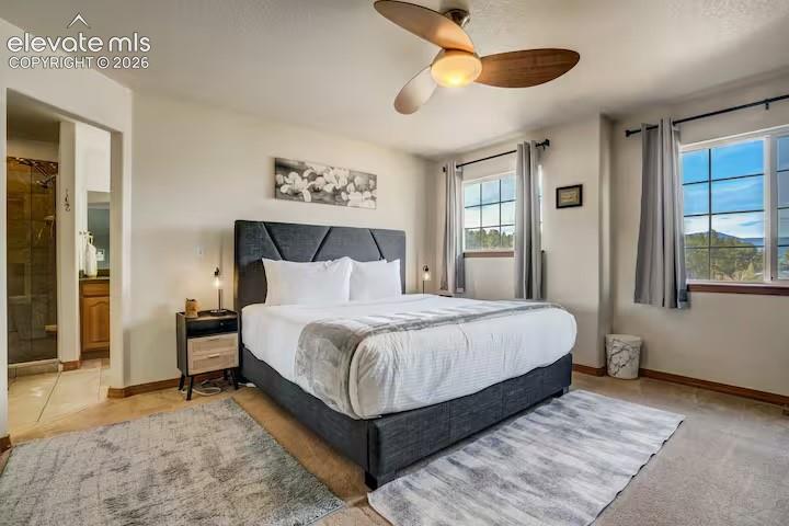 Bedroom featuring a vaulted ceiling with a wood-finish ceiling fan, two windows with grid patterns, and carpet flooring