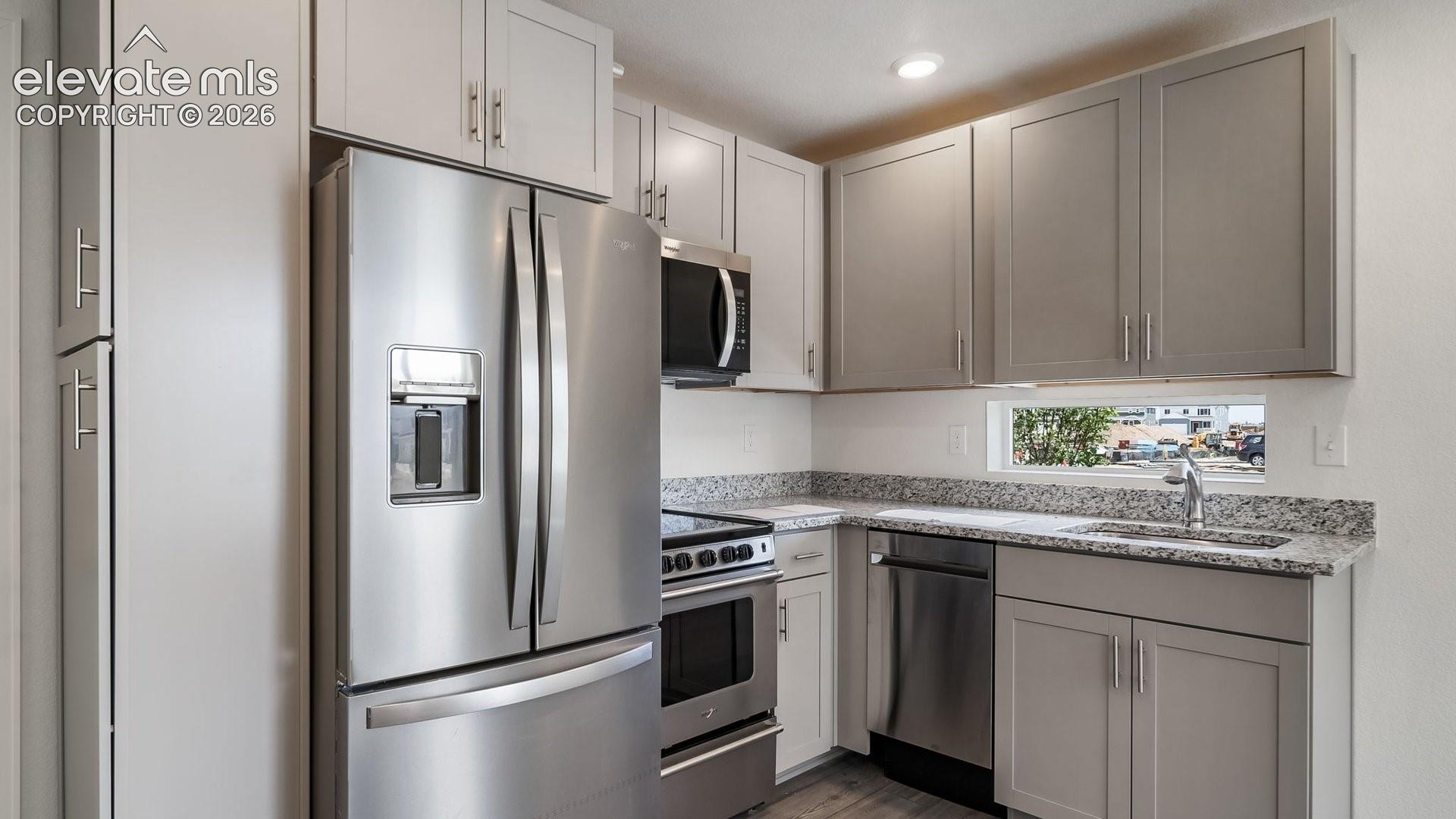 Kitchen featuring stainless steel appliances, light gray cabinetry, granite countertops, and wood-finish flooring
*photos of a model home*