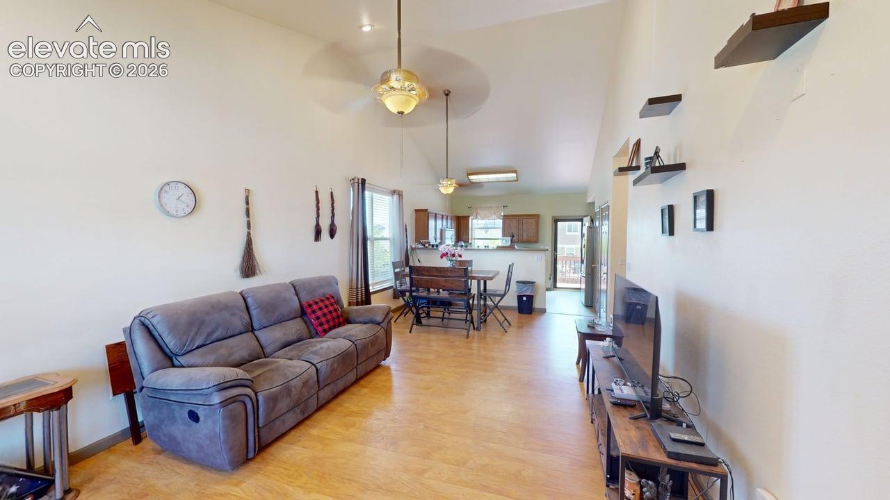 Open-concept living area with vaulted ceilings, wood-finish flooring, and a ceiling fan with integrated lighting