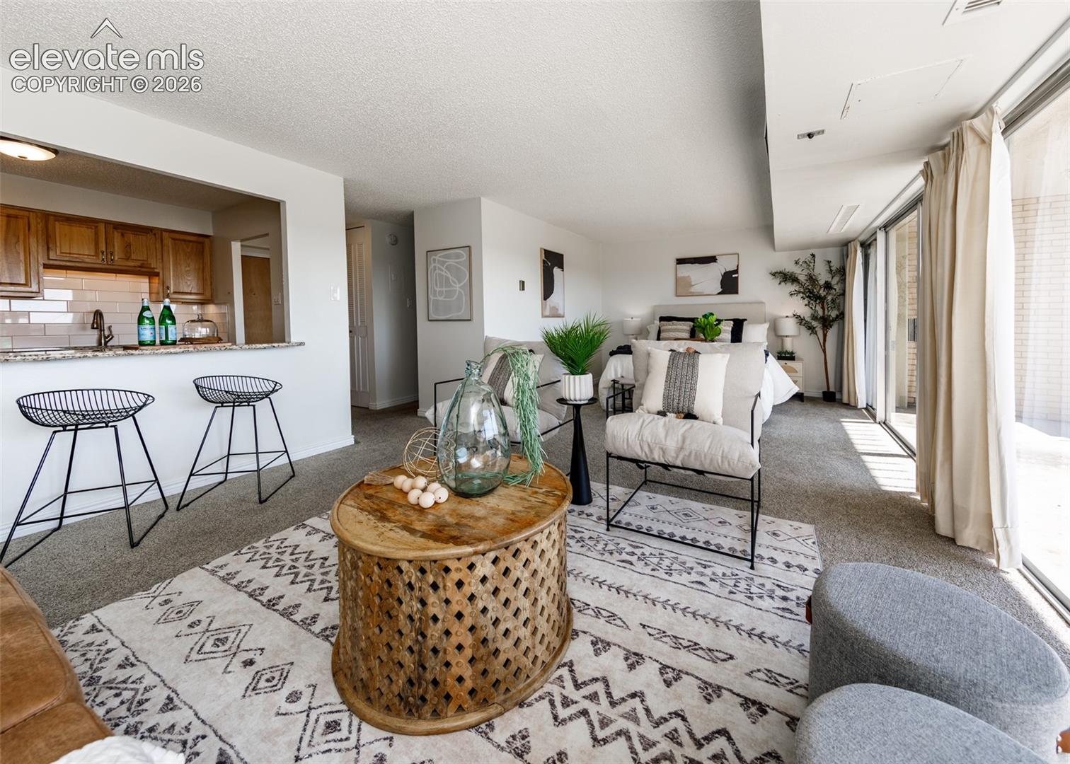Open-concept living space featuring wood-finish cabinetry, a stone-surfaced breakfast bar, and floor-to-ceiling sliding glass doors