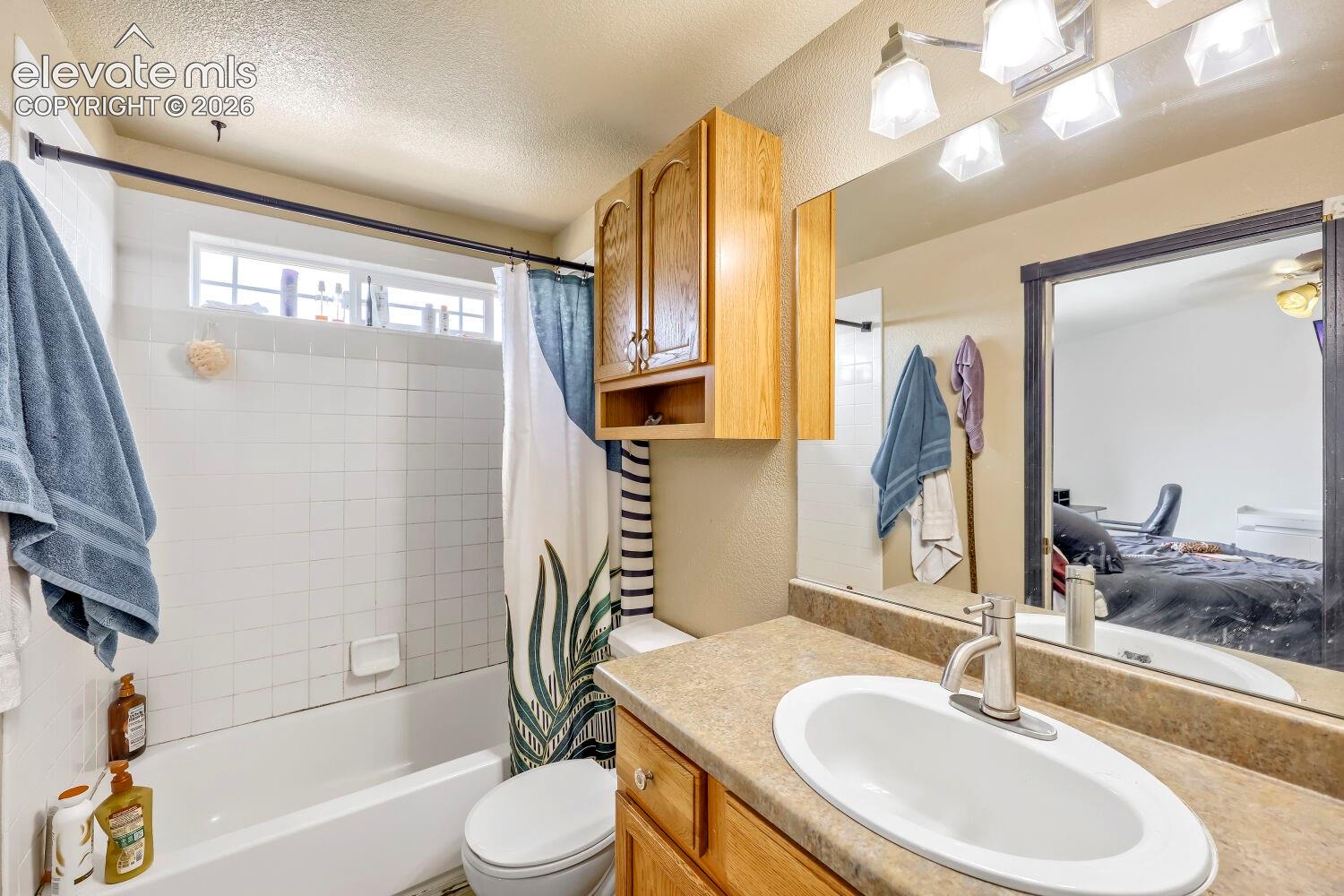 White tile shower surround with integrated bathtub, transom window, and integrated vanity with wood-finish cabinetry