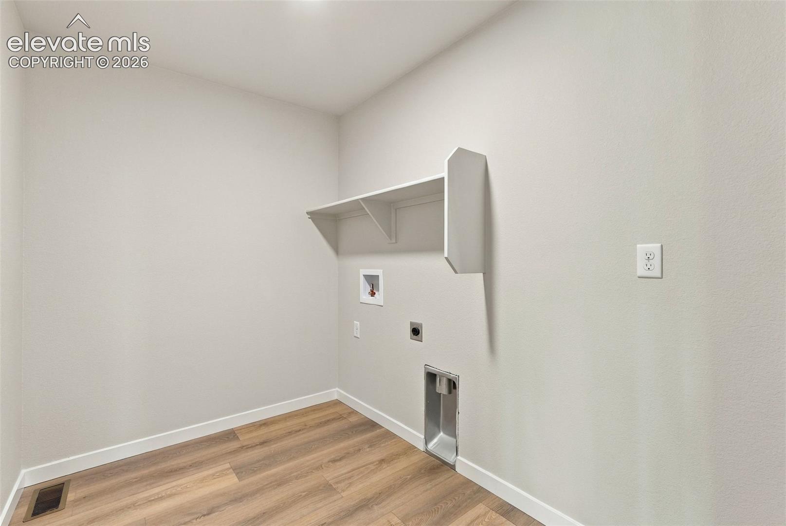 Utility area featuring wood-finish flooring, neutral wall paint, and a built-in wall shelf