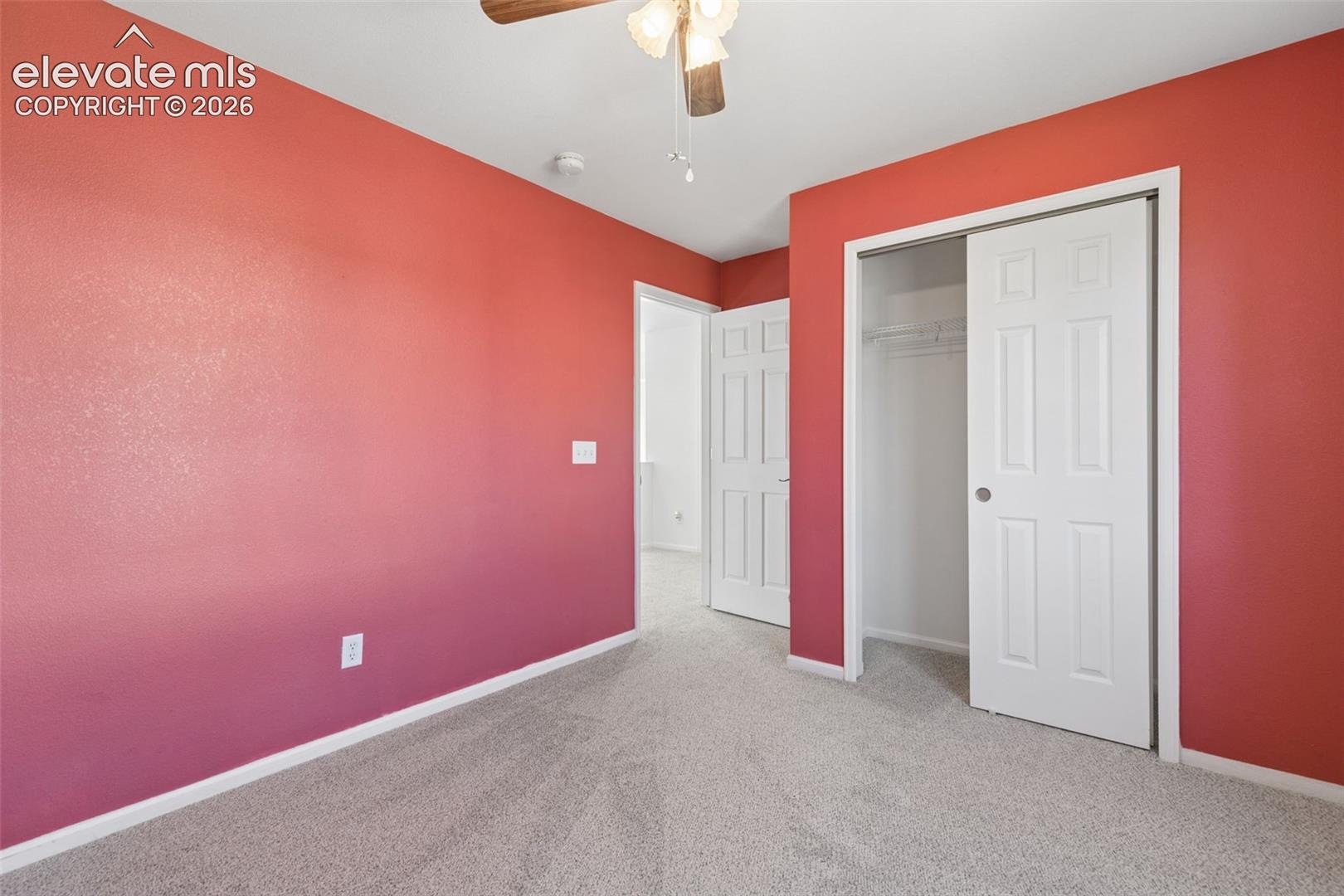 Plush carpet flooring, ceiling fan with light fixture, and sliding closet doors