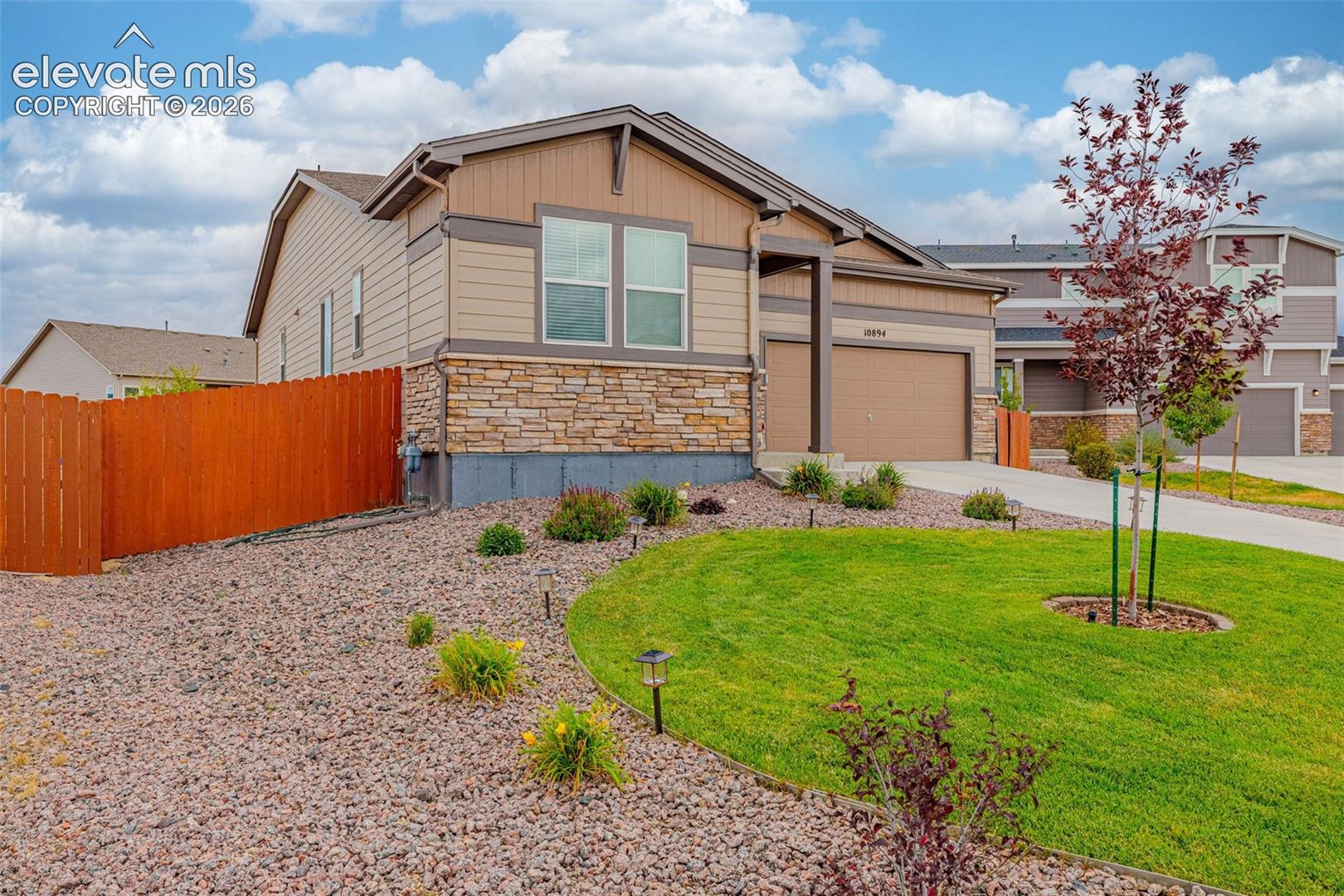 Traditional-style exterior with stone veneer accents, an attached garage, a well-maintained lawn, and a privacy fence