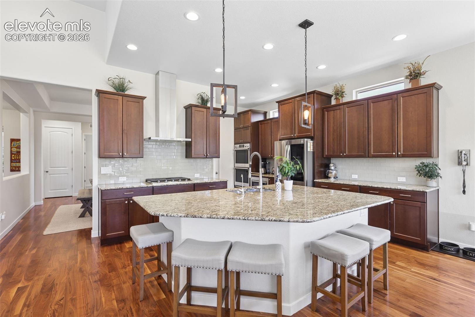Kitchen featuring rich wood-finish flooring, dark wood cabinetry, a large center island with a light-colored countertop, recessed lighting, and a stainless steel range hood