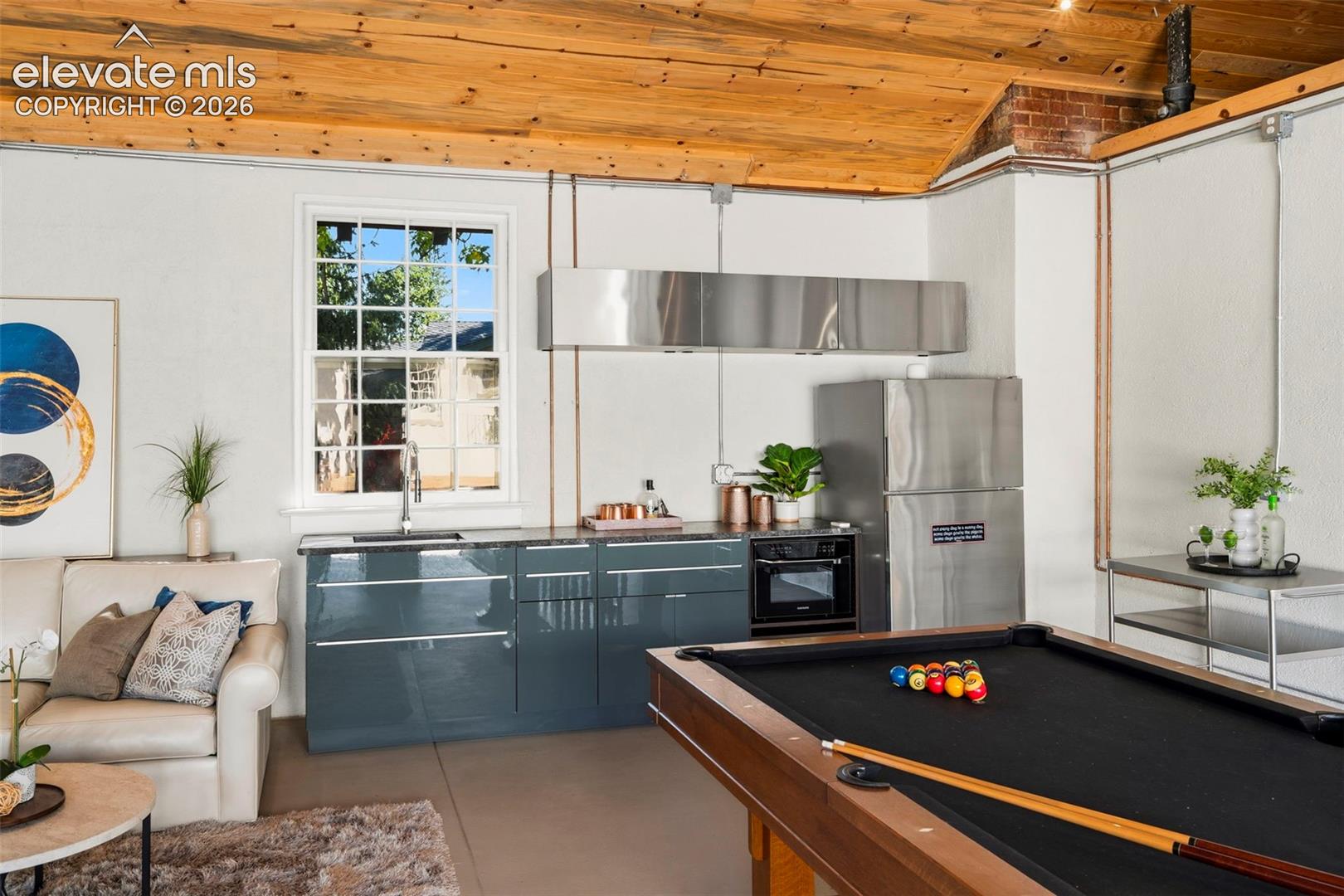 Vaulted wood-plank ceiling, exposed brick detailing, glossy charcoal cabinetry, stainless steel sink, and industrial-style stainless steel range hood