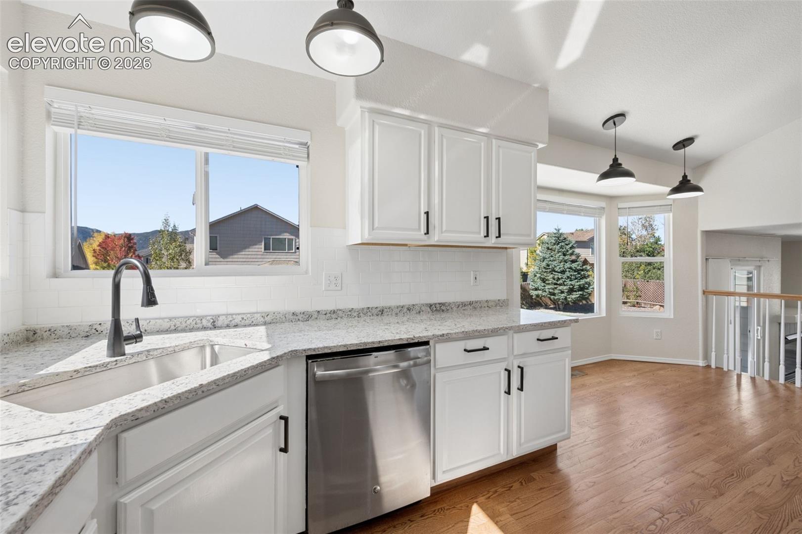 Kitchen featuring white cabinetry with matte black hardware, stone-patterned countertops, stainless steel dishwasher, white subway tile backsplash, and wood-finish flooring