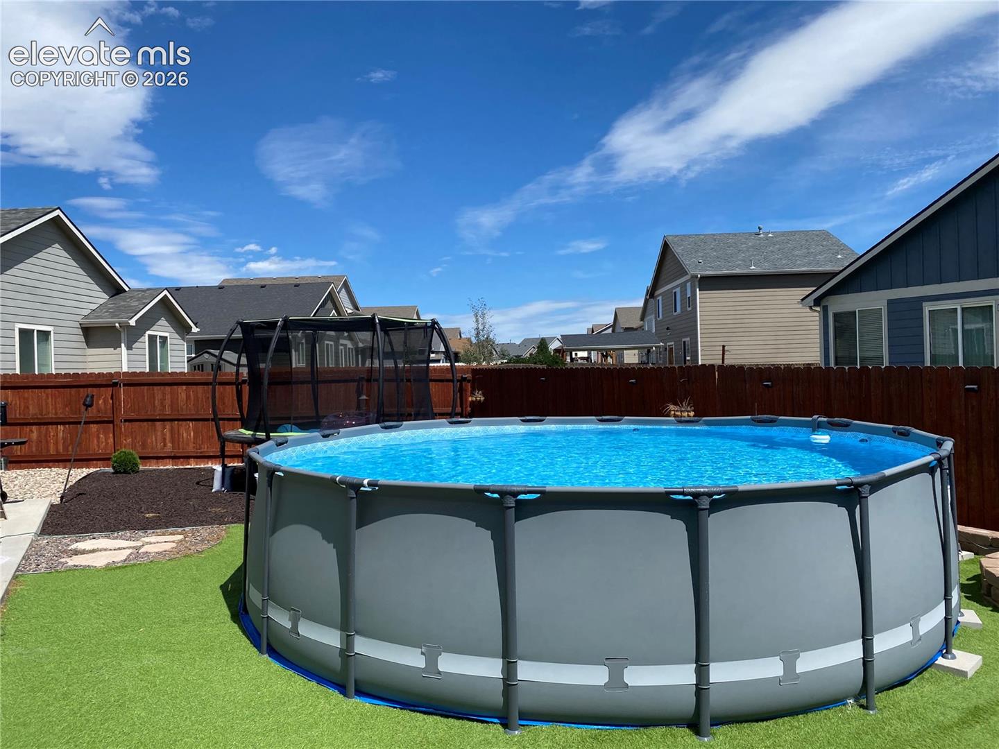 Backyard featuring an above-ground pool, artificial turf, wood fencing, and a mulched bed