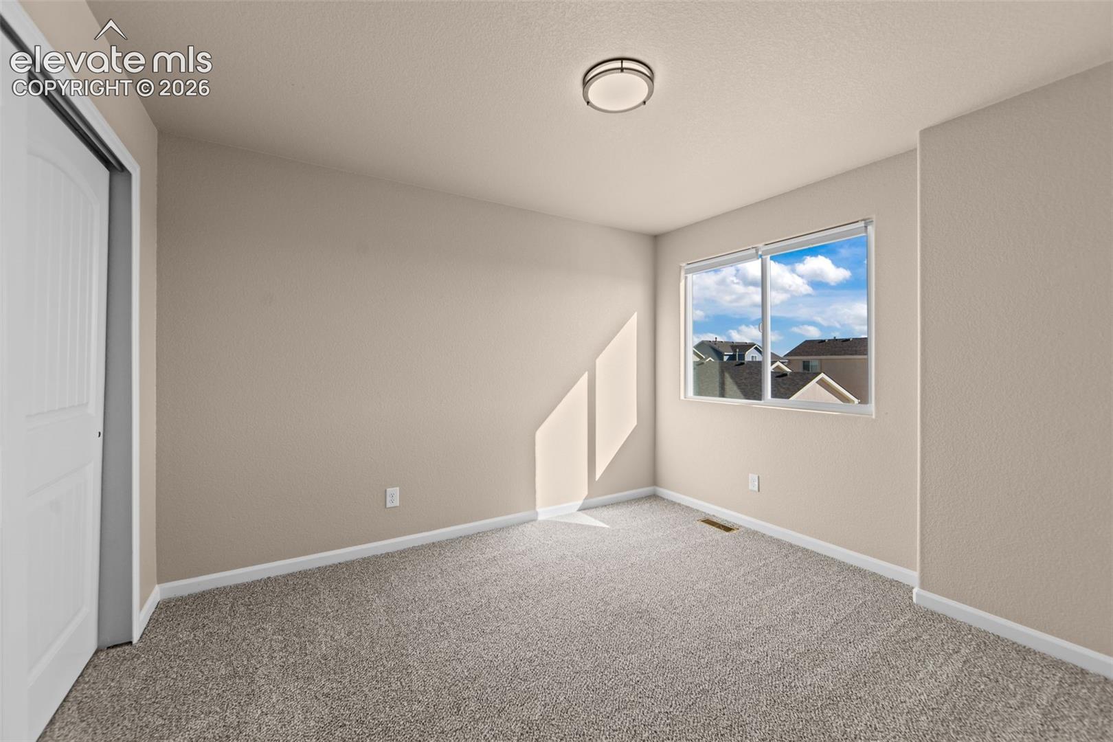 Neutral-toned interior featuring wall-to-wall carpeting, a sliding panel door, a double-pane window, and a circular flush-mount ceiling light