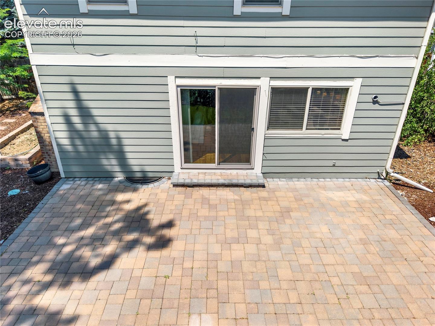 Paver patio with horizontal lap siding, sliding glass door, and sliding window